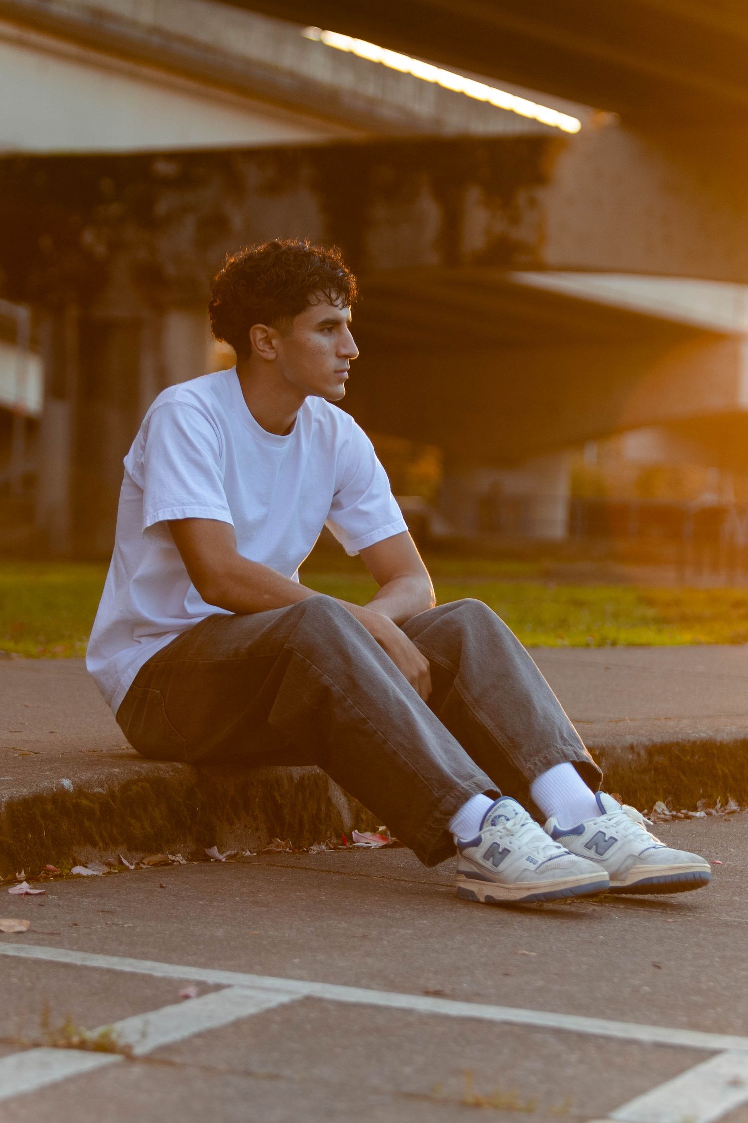 A person in a white t-shirt and dark pants sits on the ground at sunset, creating a contemplative silhouette.