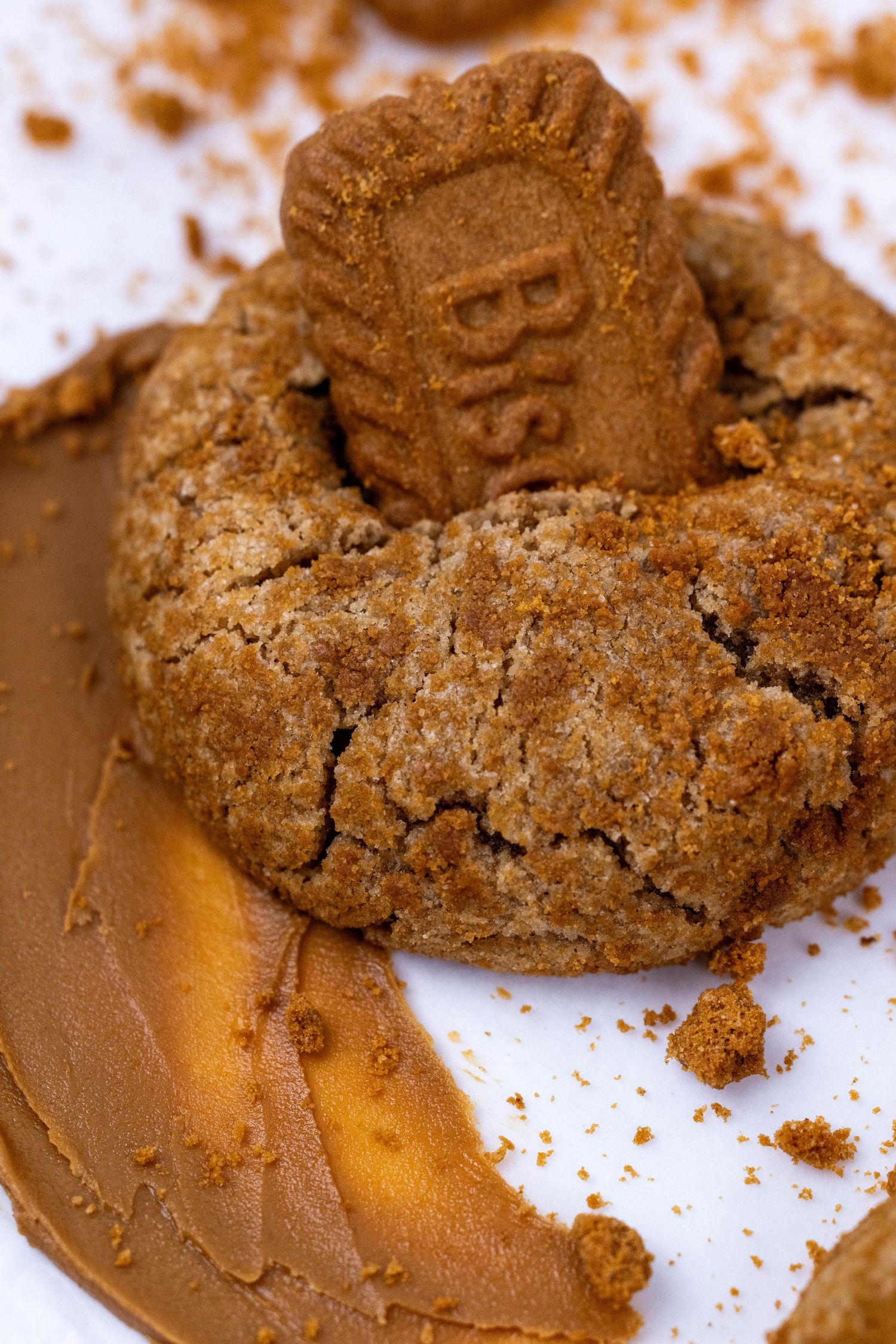 A crumbled chocolate cookie with Biscoff spread and cookie pieces scattered on a white surface.