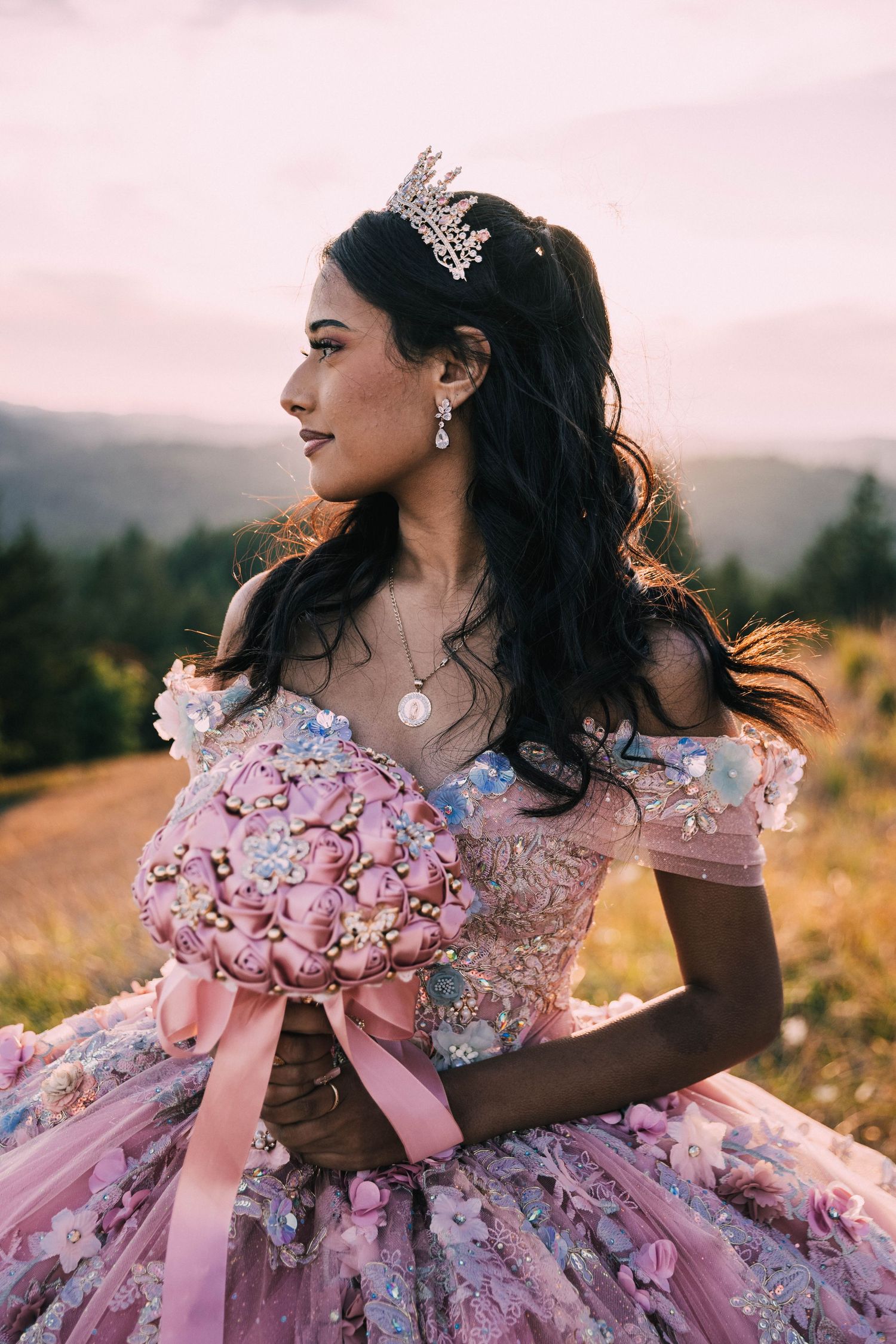 A dreamy outdoor portrait featuring someone in an ornate pink ball gown with floral details at sunset.