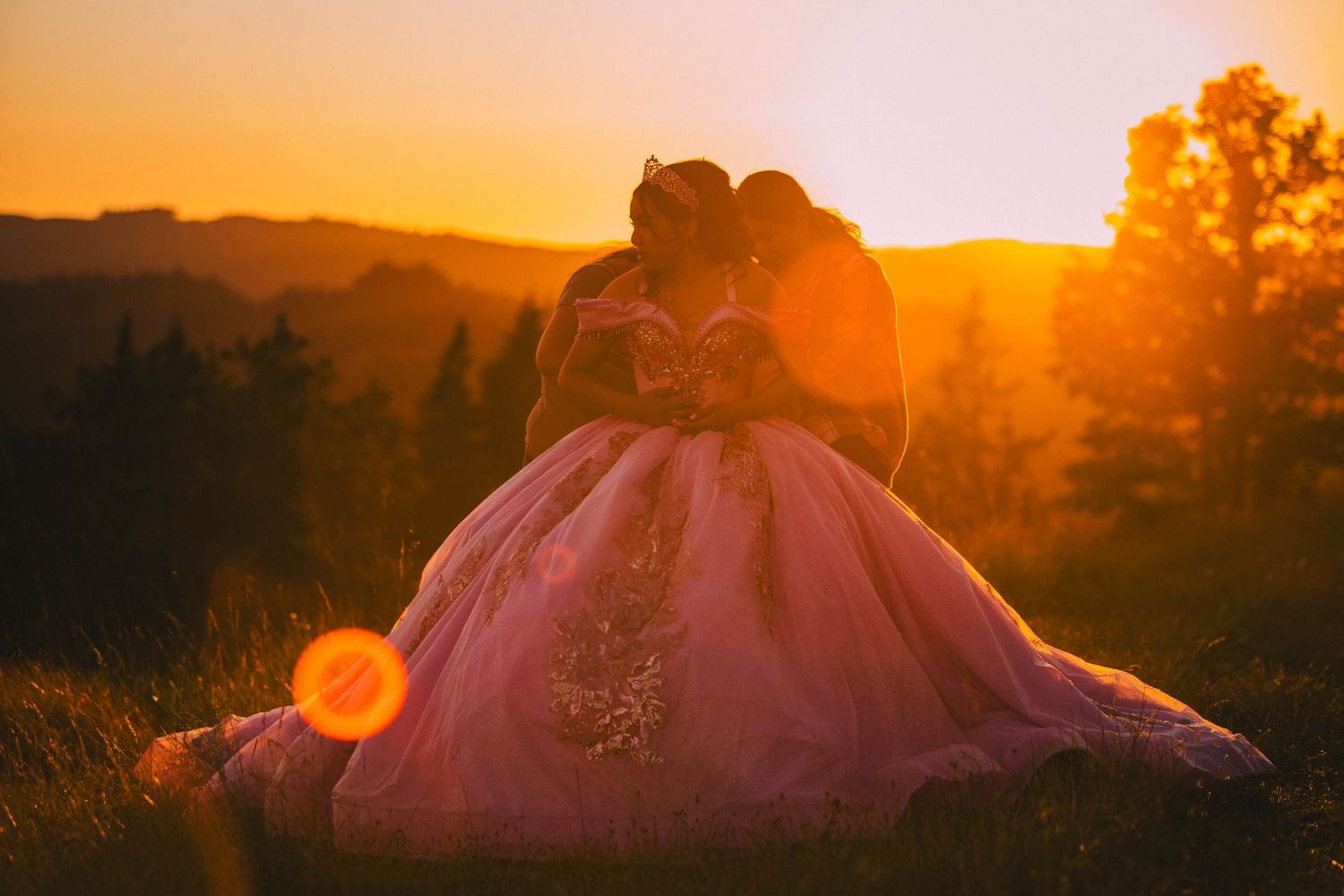Dramatic sunset silhouettes rolling hills and mountains with golden orange sky and lens flare.