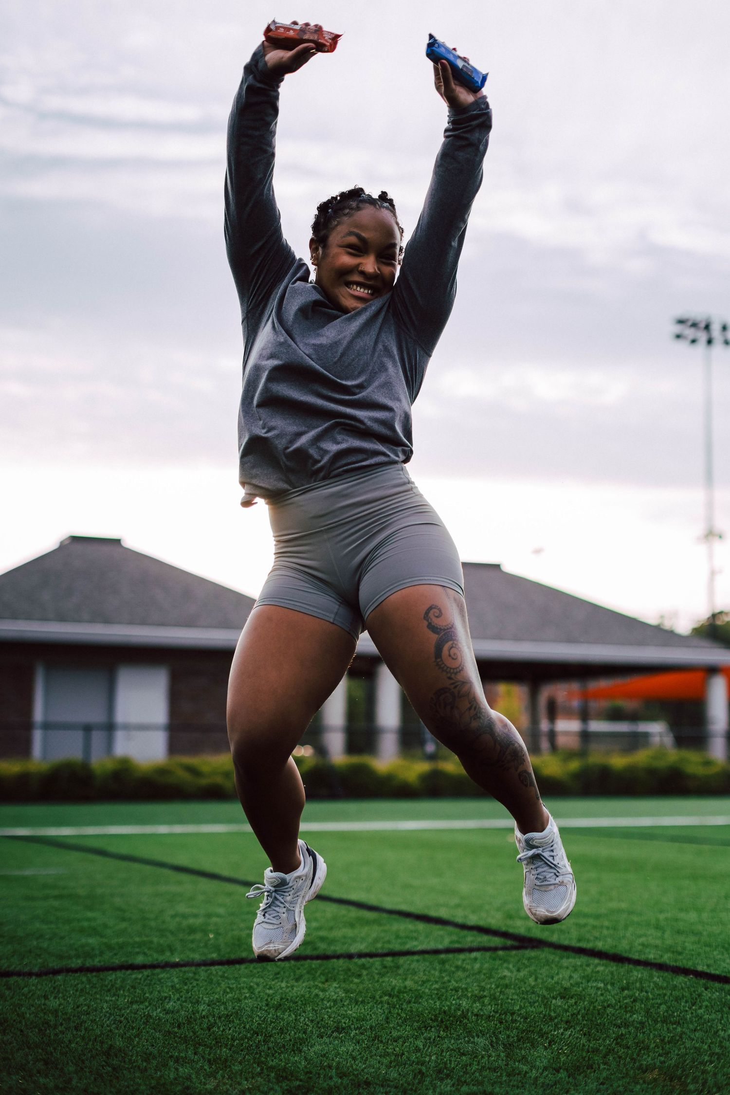 A person in gray athletic wear performs dynamic stretching exercises on an outdoor turf field at sunset.