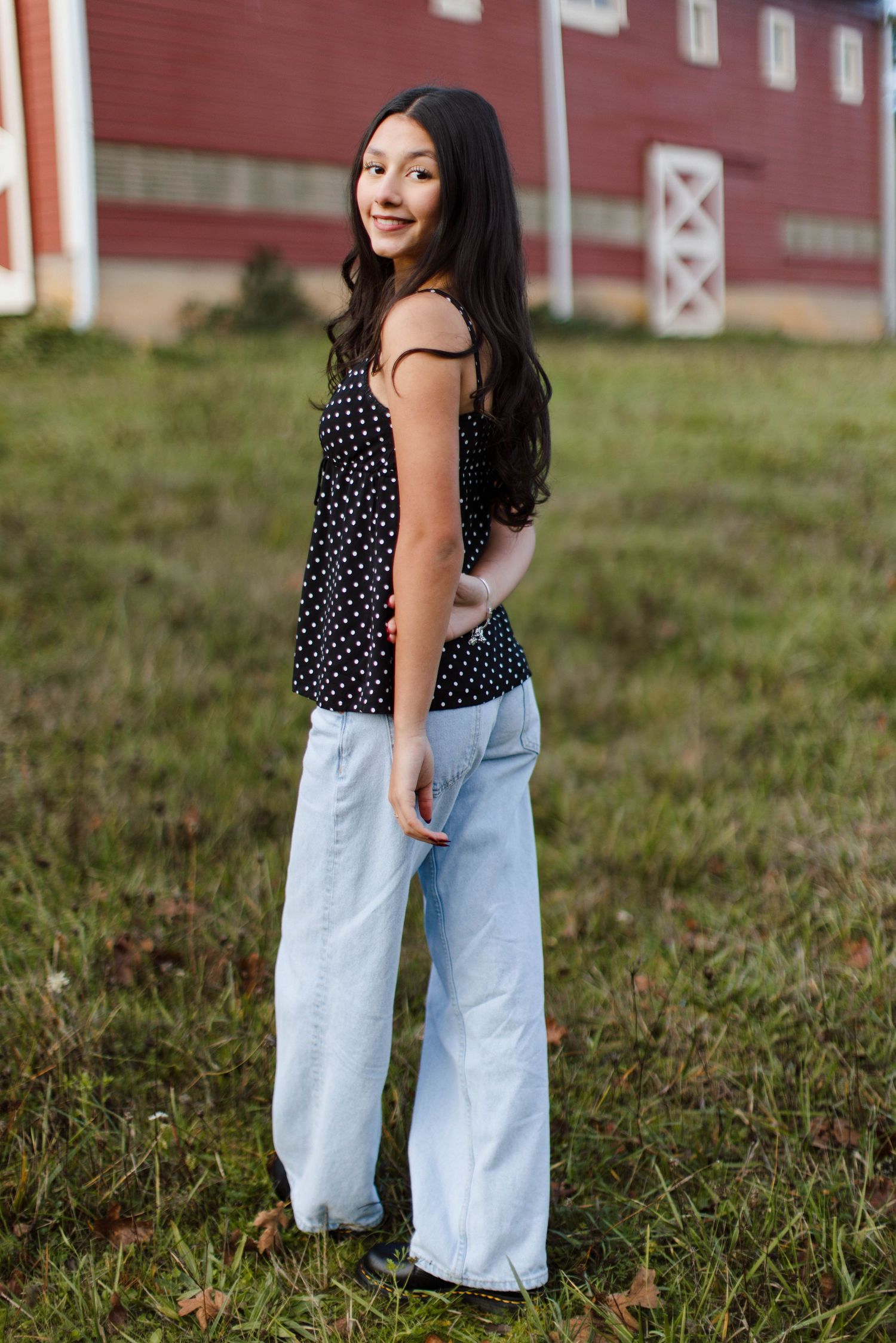 A polka dot top and light wash jeans outfit photographed in front of a rustic red barn.