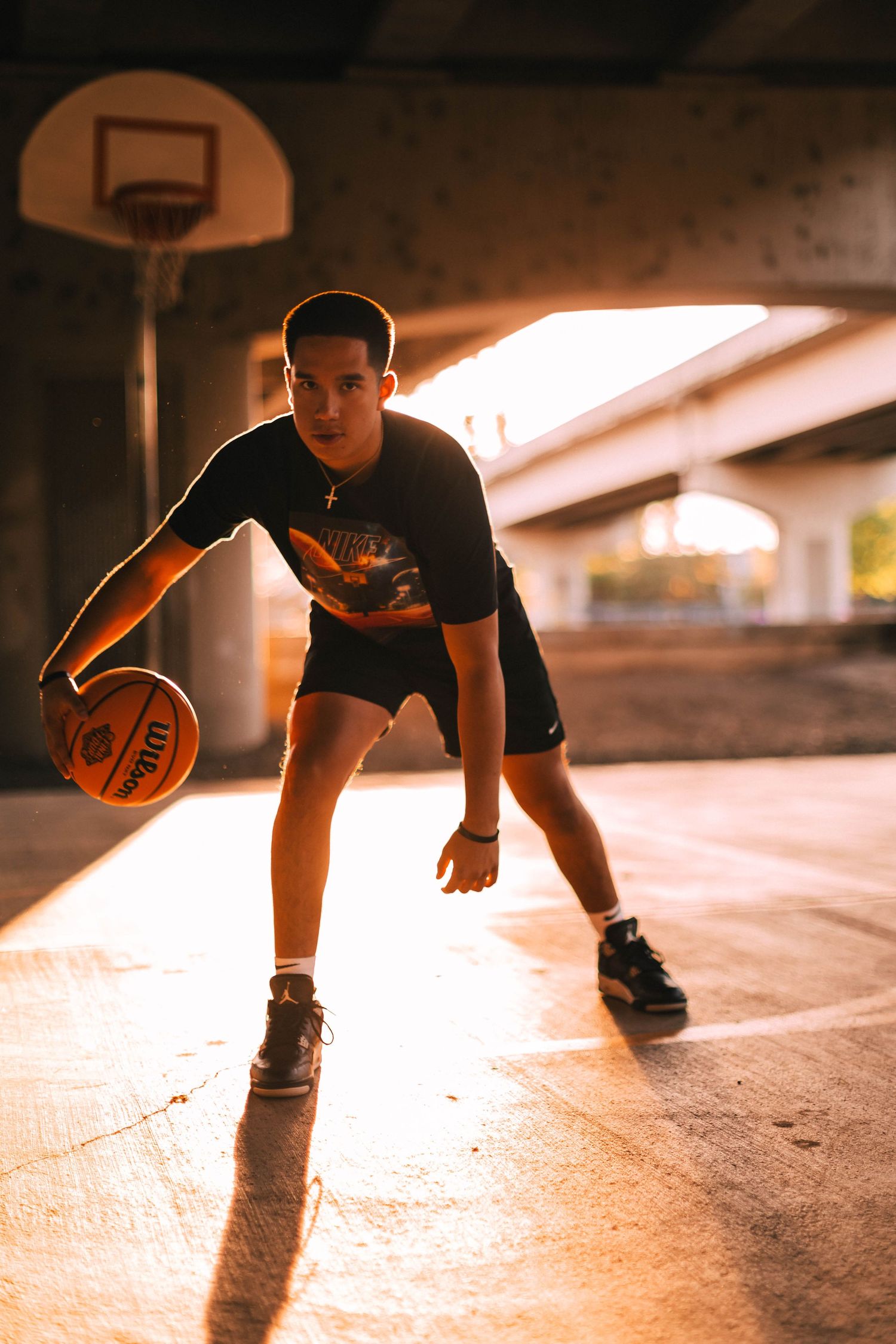 Basketball player dribbling on concrete court at sunset with dramatic lighting and long shadows.