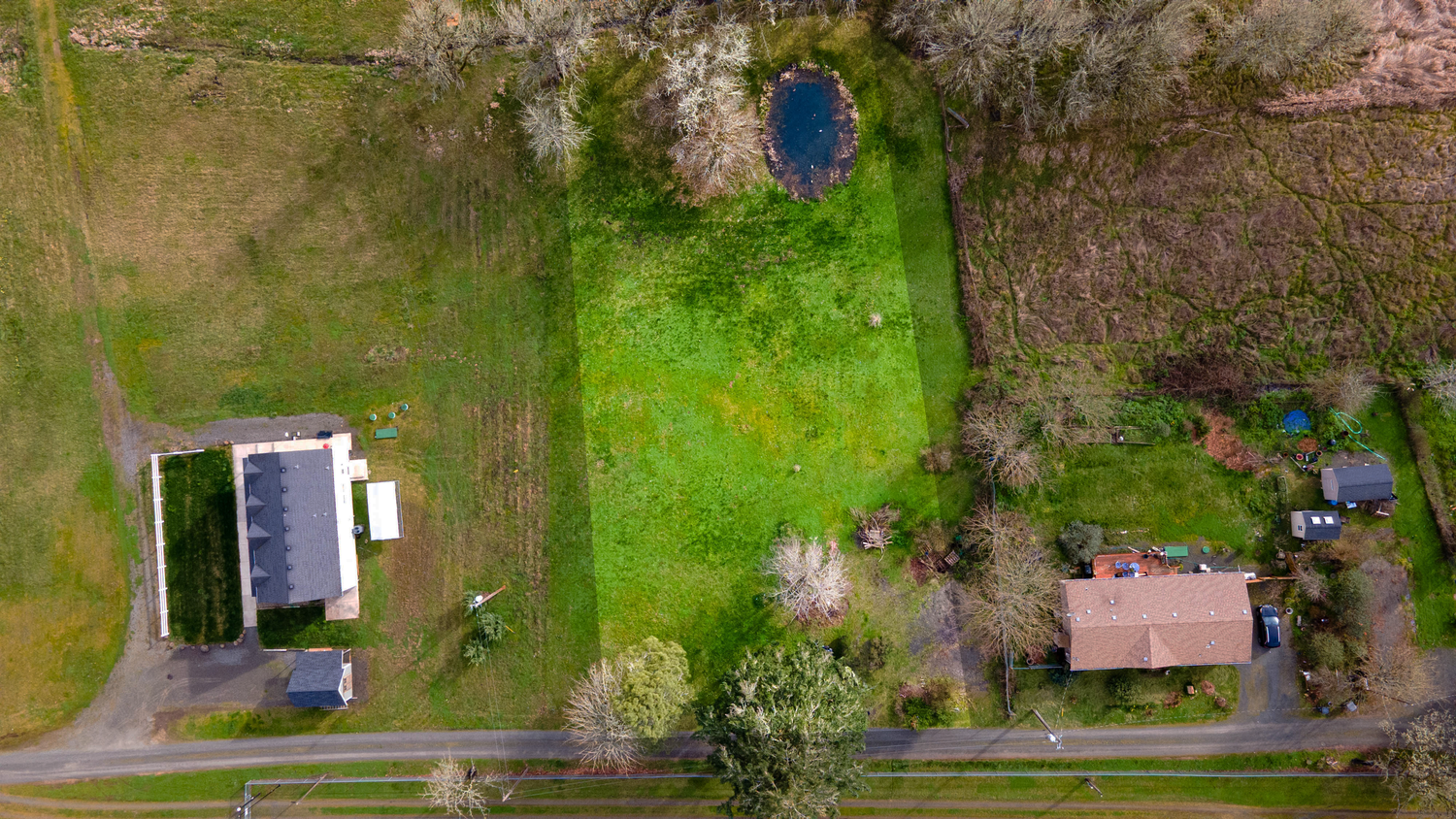 Aerial view of a long residential driveway with green lawns and trees on both sides during spring or summer.