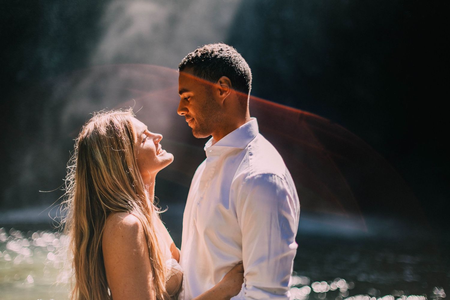 Intimate couple shares tender moments by a scenic woodland creek in natural lighting.