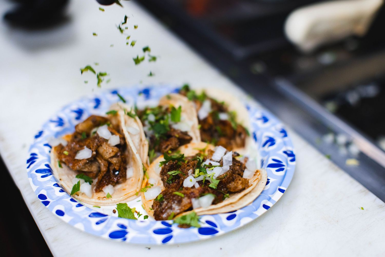 Freshly prepared tacos with meat, cilantro and onions served on decorative blue and white plates.
