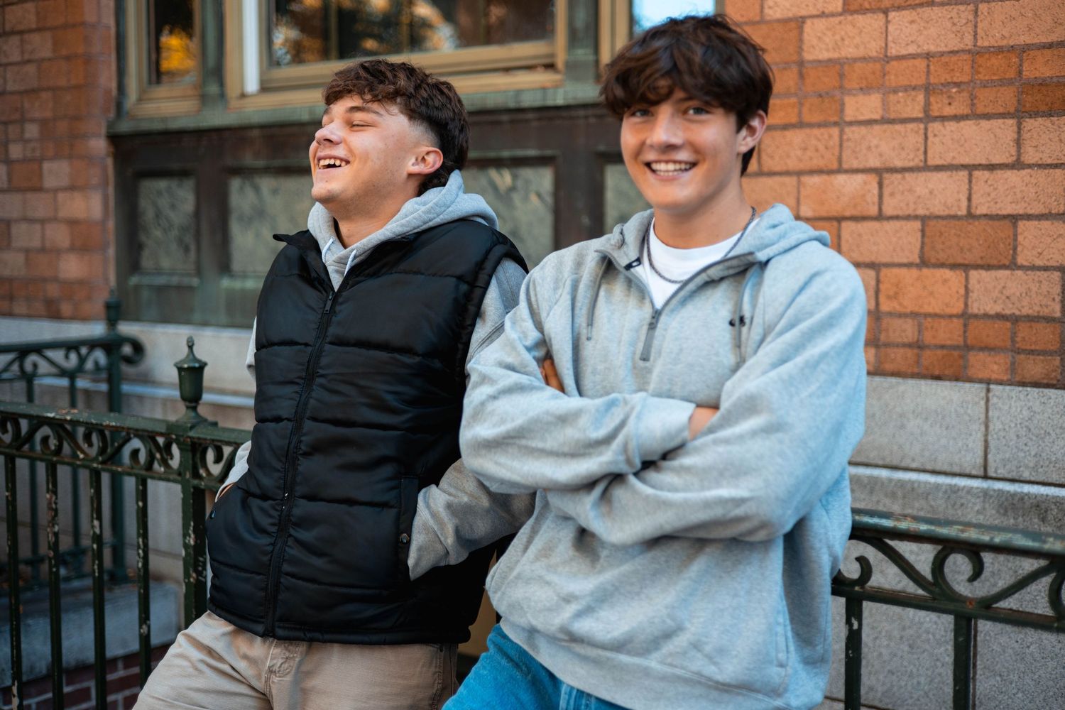 Two people share a candid laughing moment together while standing outside a brick building.