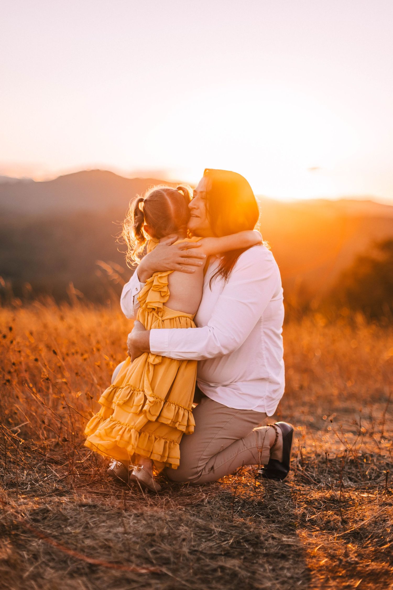 A tender embrace between parent and child in a golden wheat field at sunset creates a heartwarming silhouette.
