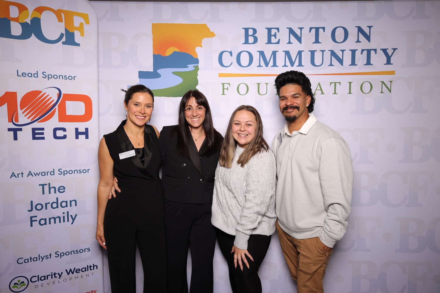 Group photo of people posing together at a corporate event with sponsor banners and logos visible in background.