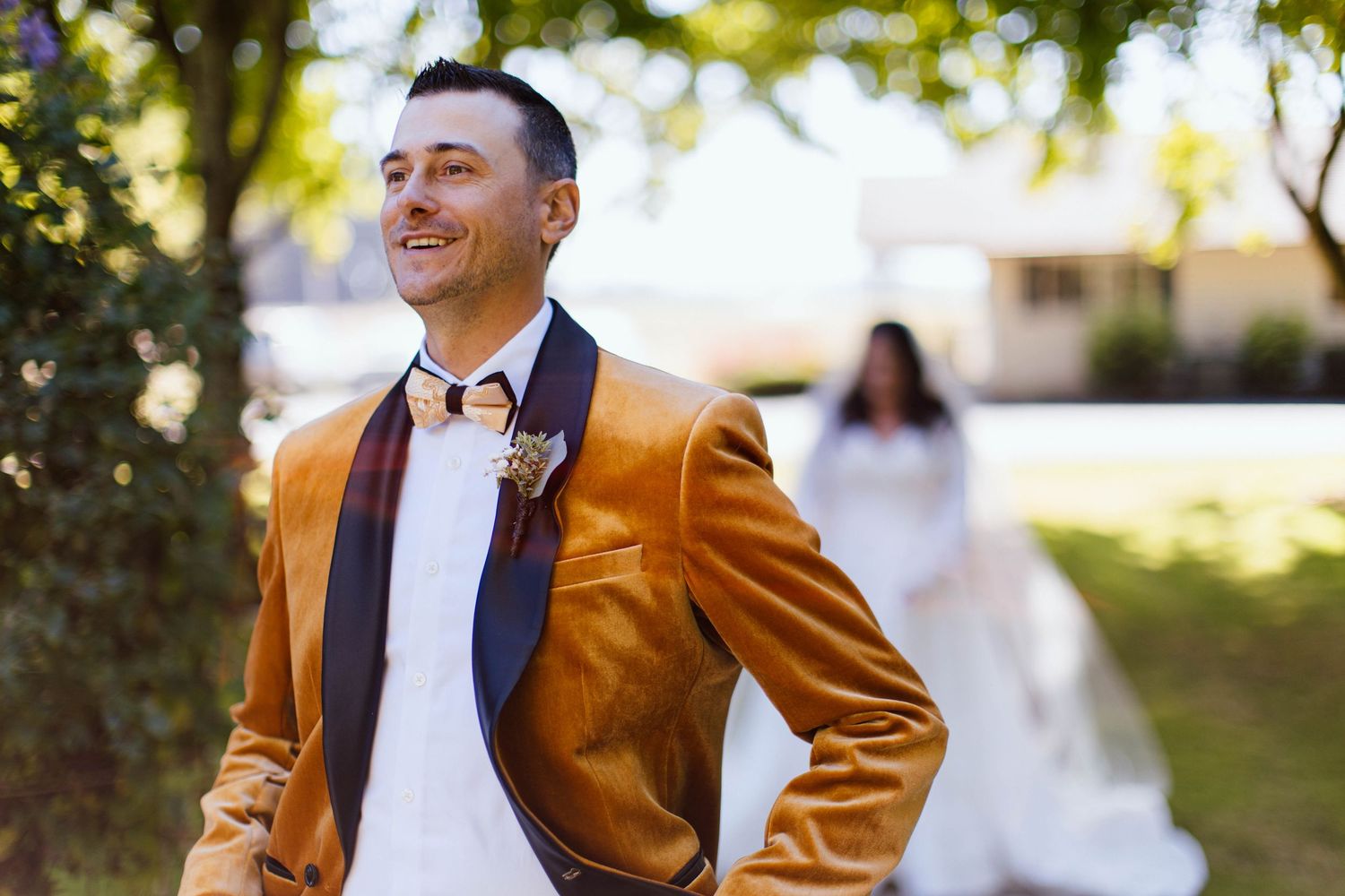 A person wearing a brown blazer and white shirt poses outdoors in a garden setting.