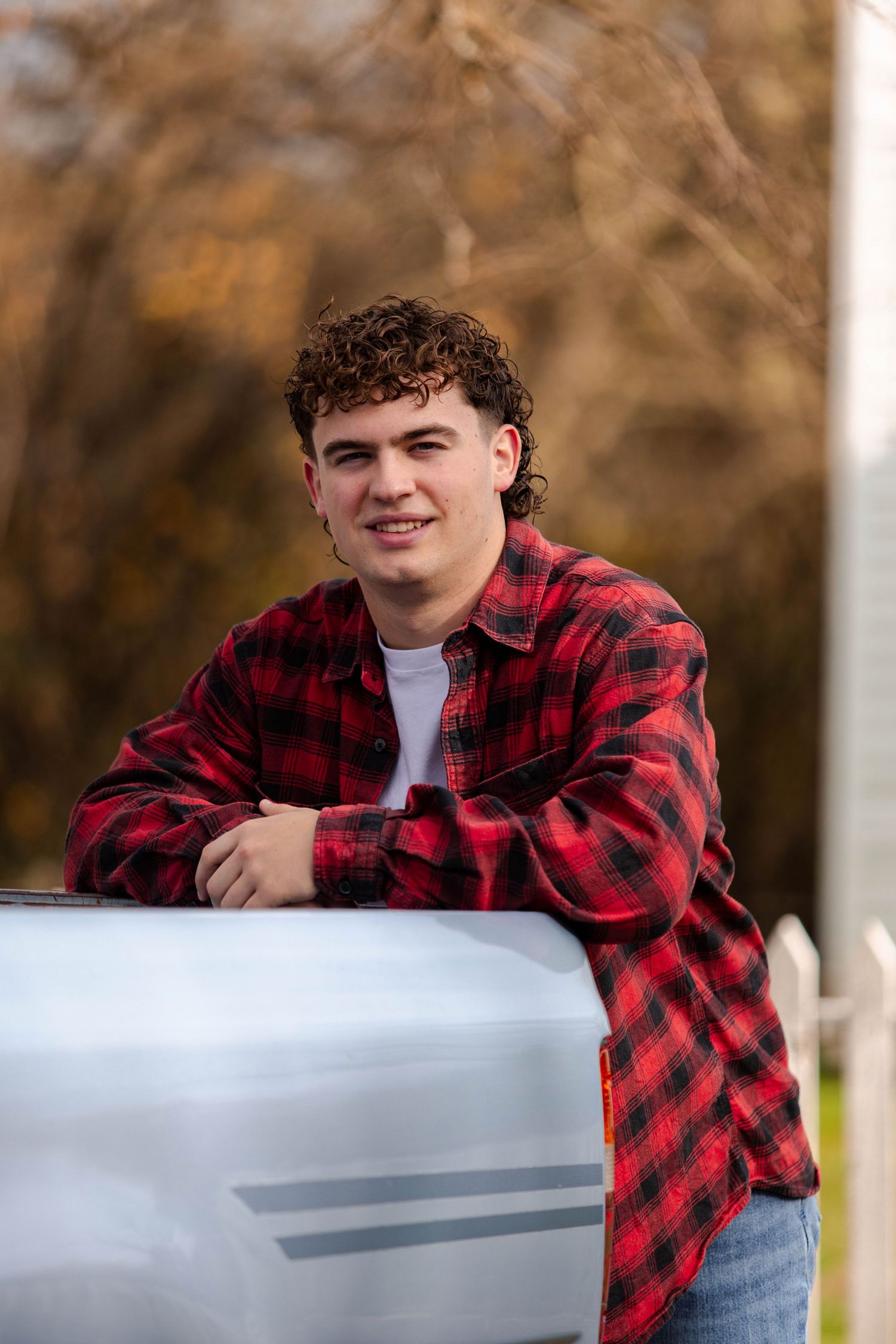 Outdoor portrait of someone wearing a red and black buffalo plaid flannel shirt leaning on a metal surface.