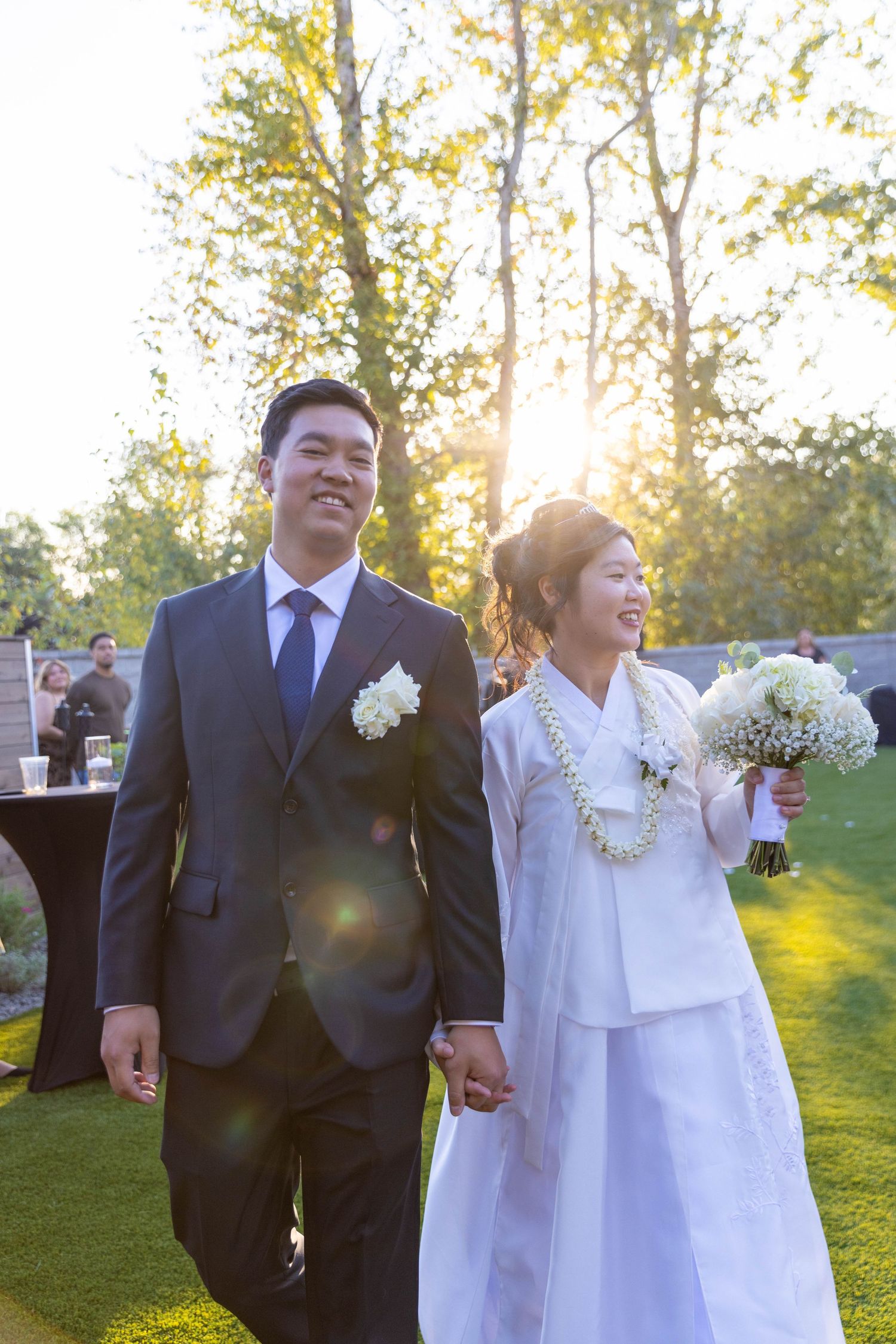 Wedding couple walks arm in arm through a sun-drenched garden during golden hour celebration.