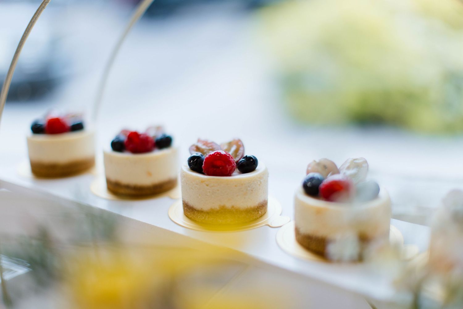 A row of mini cheesecakes topped with fresh berries arranged on a white surface in natural lighting.