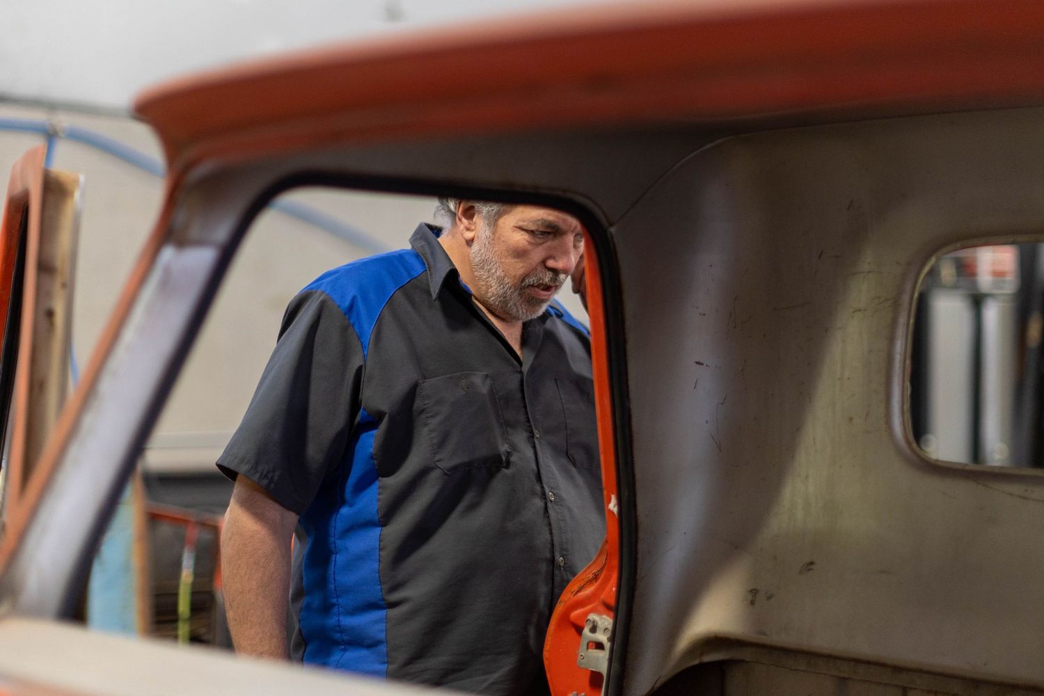 Person in a dark shirt and blue vest operates machinery controls inside an industrial vehicle cabin.