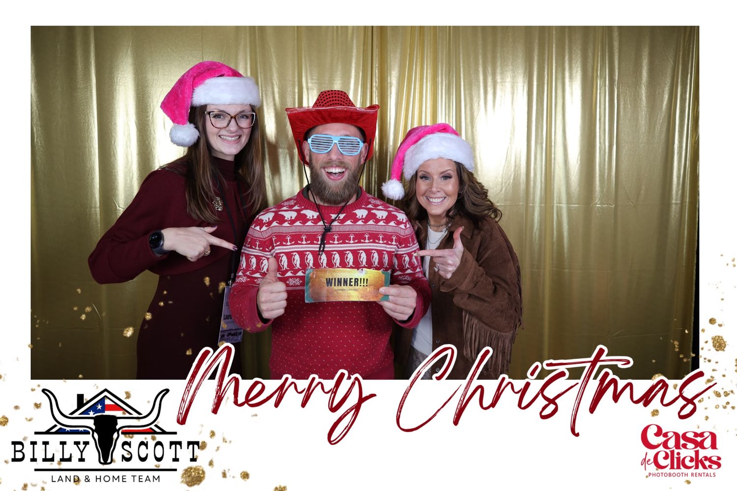 Three people in Santa hats pose with a festive photo prop against a gold backdrop at a holiday photo booth.