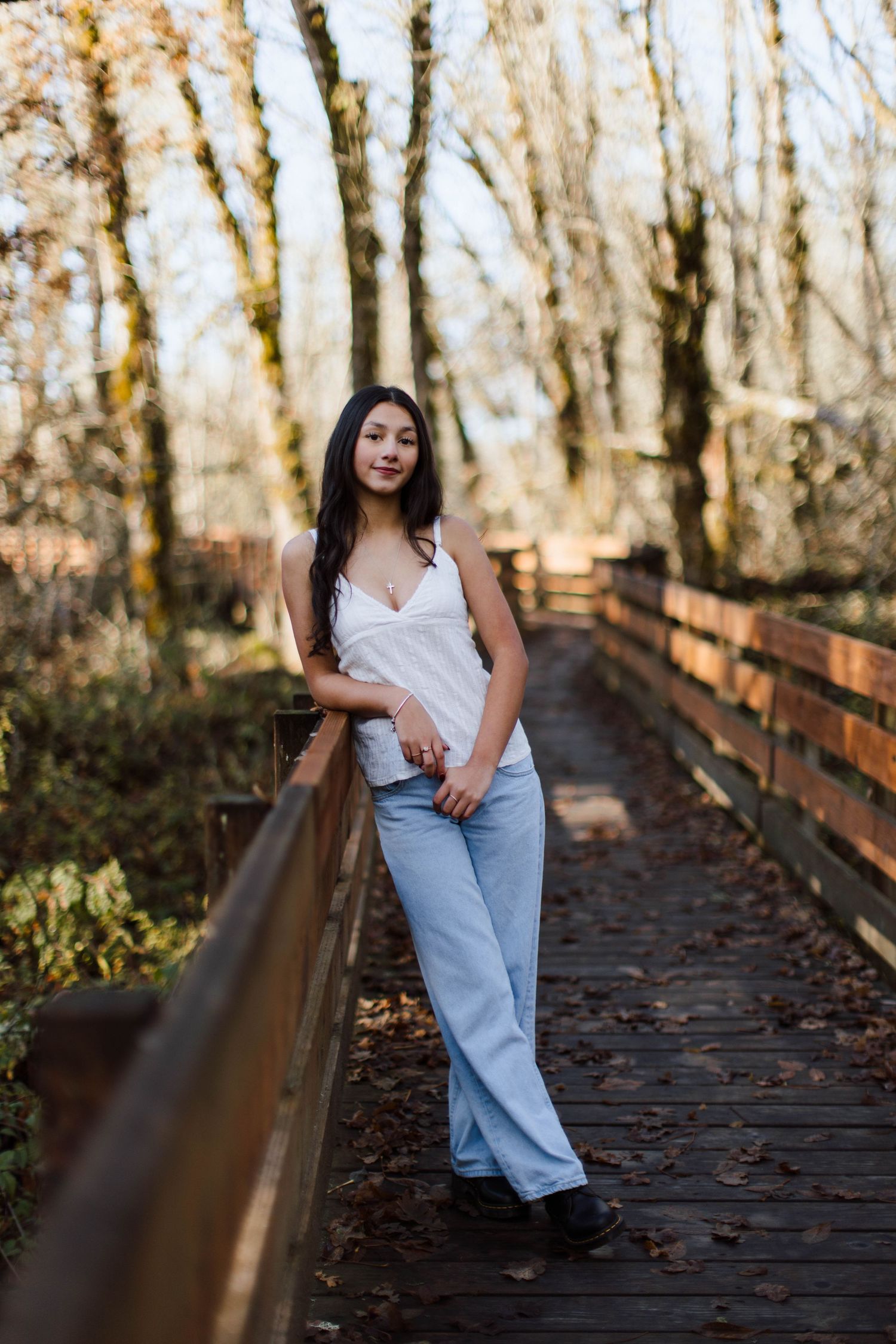 A figure poses on a wooden boardwalk surrounded by autumn trees in natural lighting.