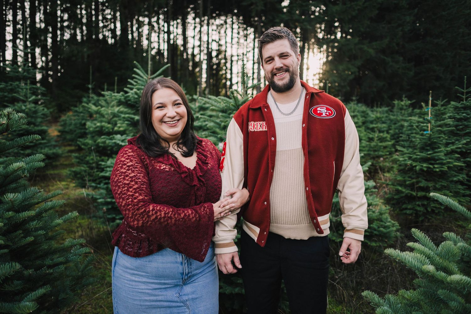 Romantic couple embraces while surrounded by tall evergreen trees in an outdoor forest setting.