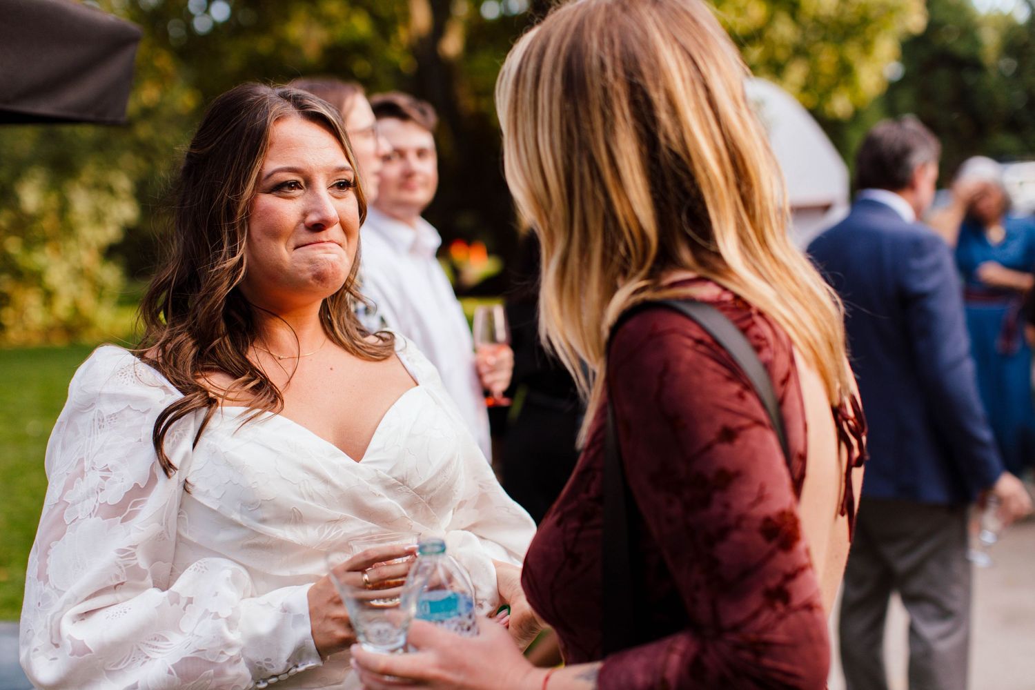 Two people share a warm embrace during an outdoor celebration while others gather in the background.