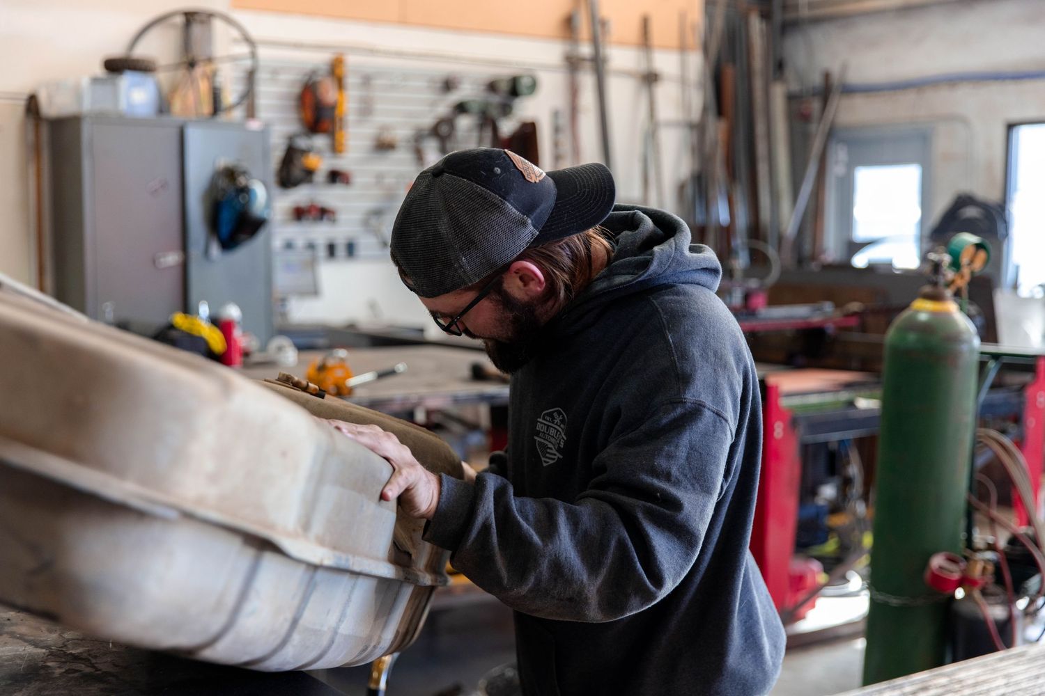 Craftsperson in protective gear working on a large piece of metal in a workshop.