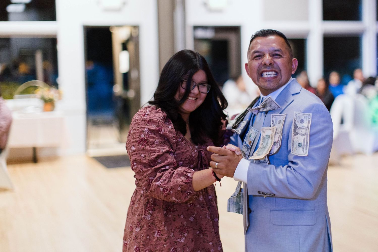 Two people share a joyful dance moment together at an indoor venue, with one wearing a floral dress and another in blue attire.