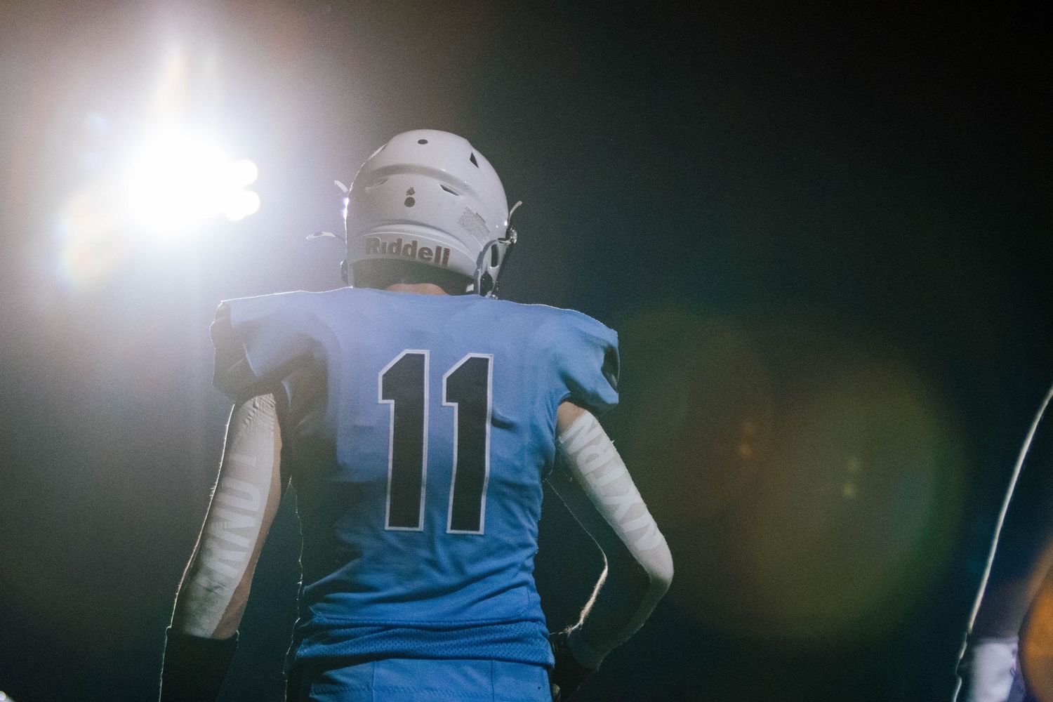 A football player in blue and white uniform runs across the field during a game under stadium lights.