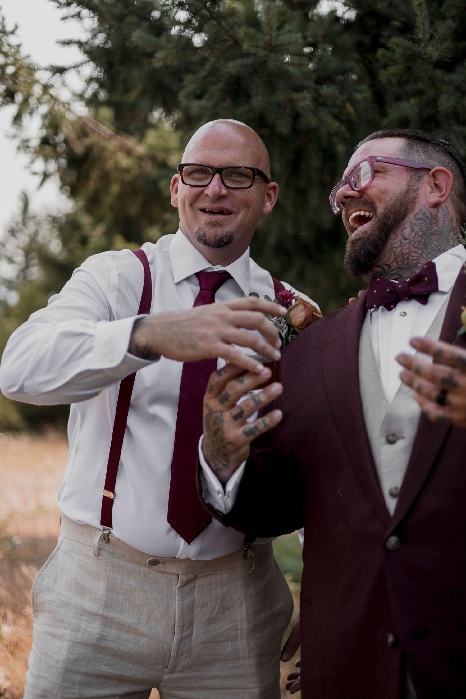 Wedding party members in burgundy and white attire share a celebratory toast outdoors.