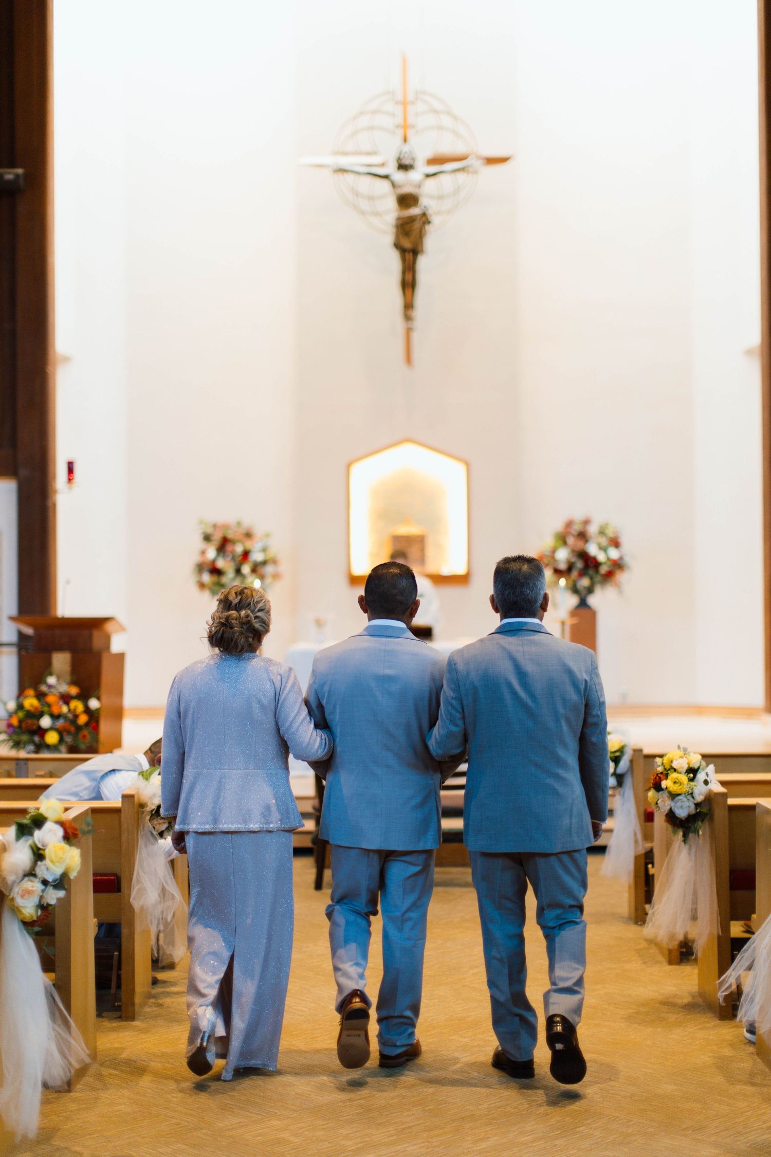Groomsmen in matching blue suits stand in a row at the altar of a church during a wedding ceremony.