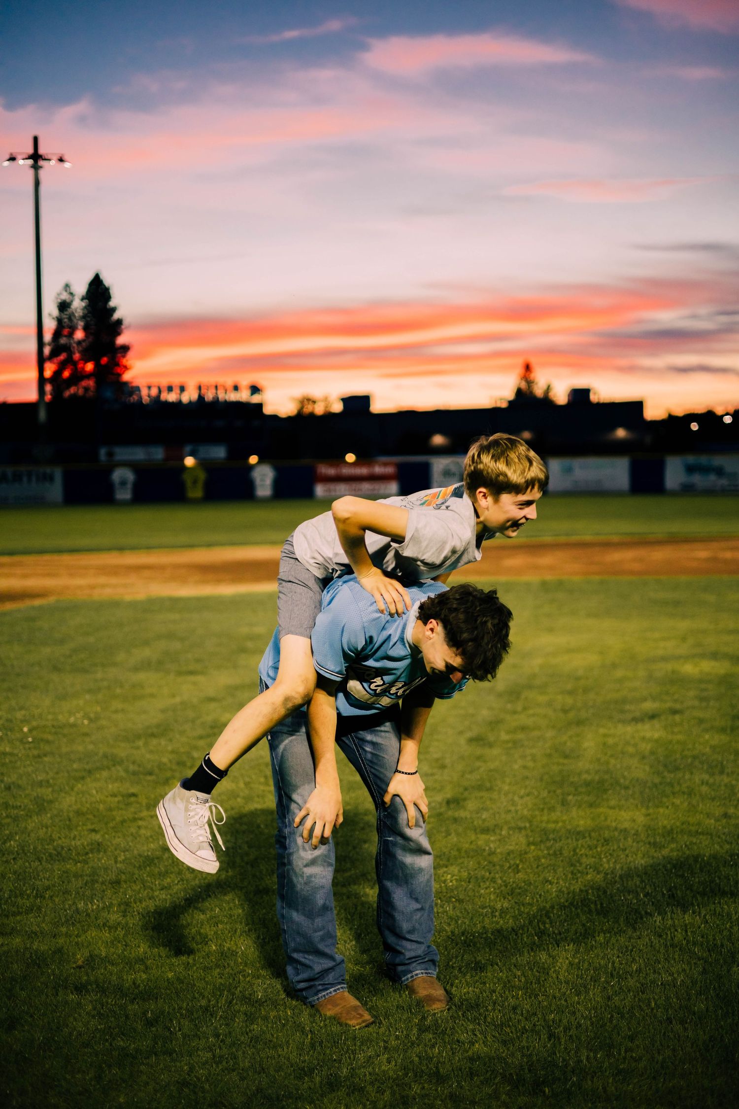 Two people playfully interacting on a baseball field during a vibrant sunset.