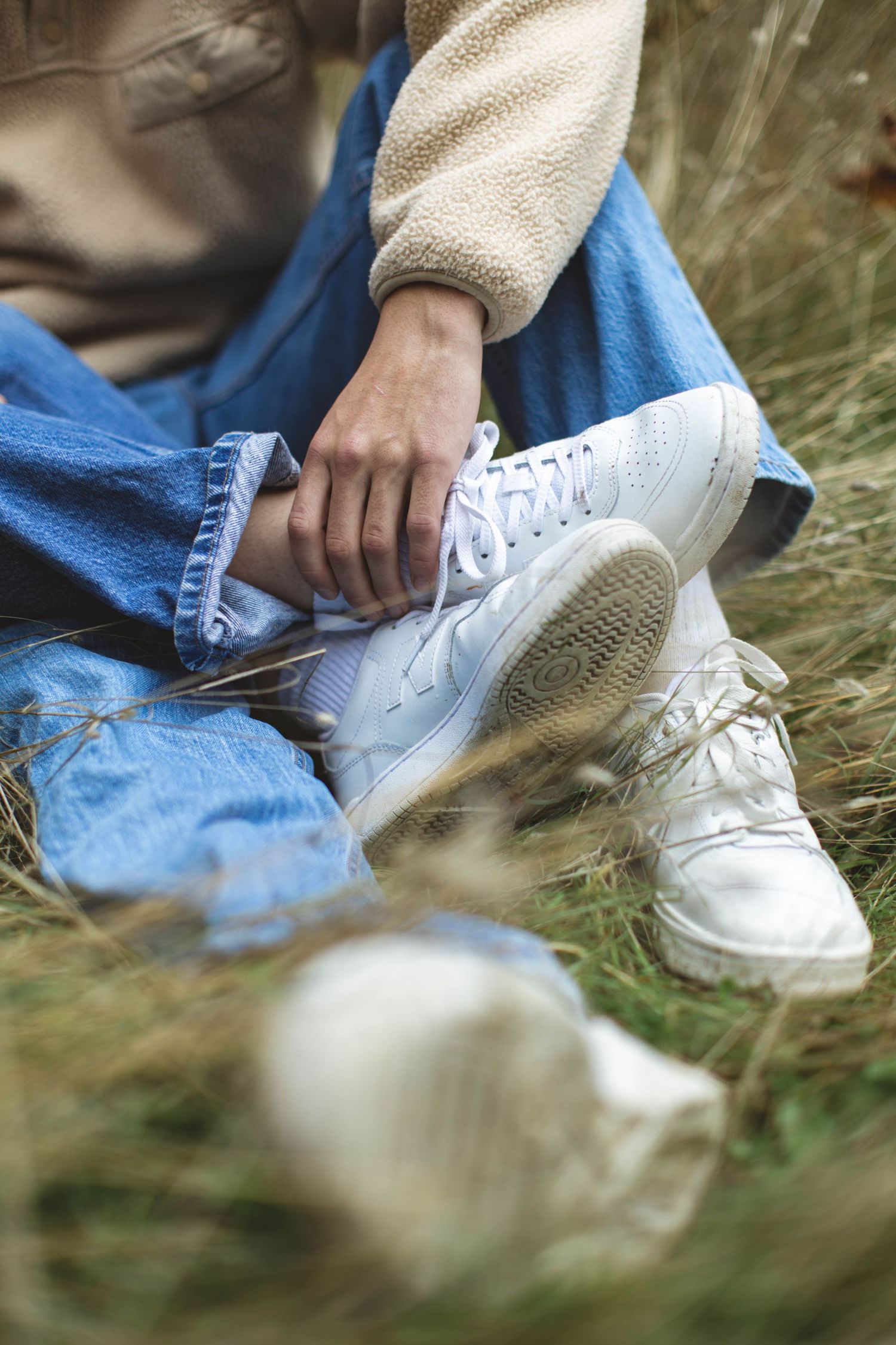 Close-up sequence of someone tying white canvas sneakers while sitting in grass outdoors.