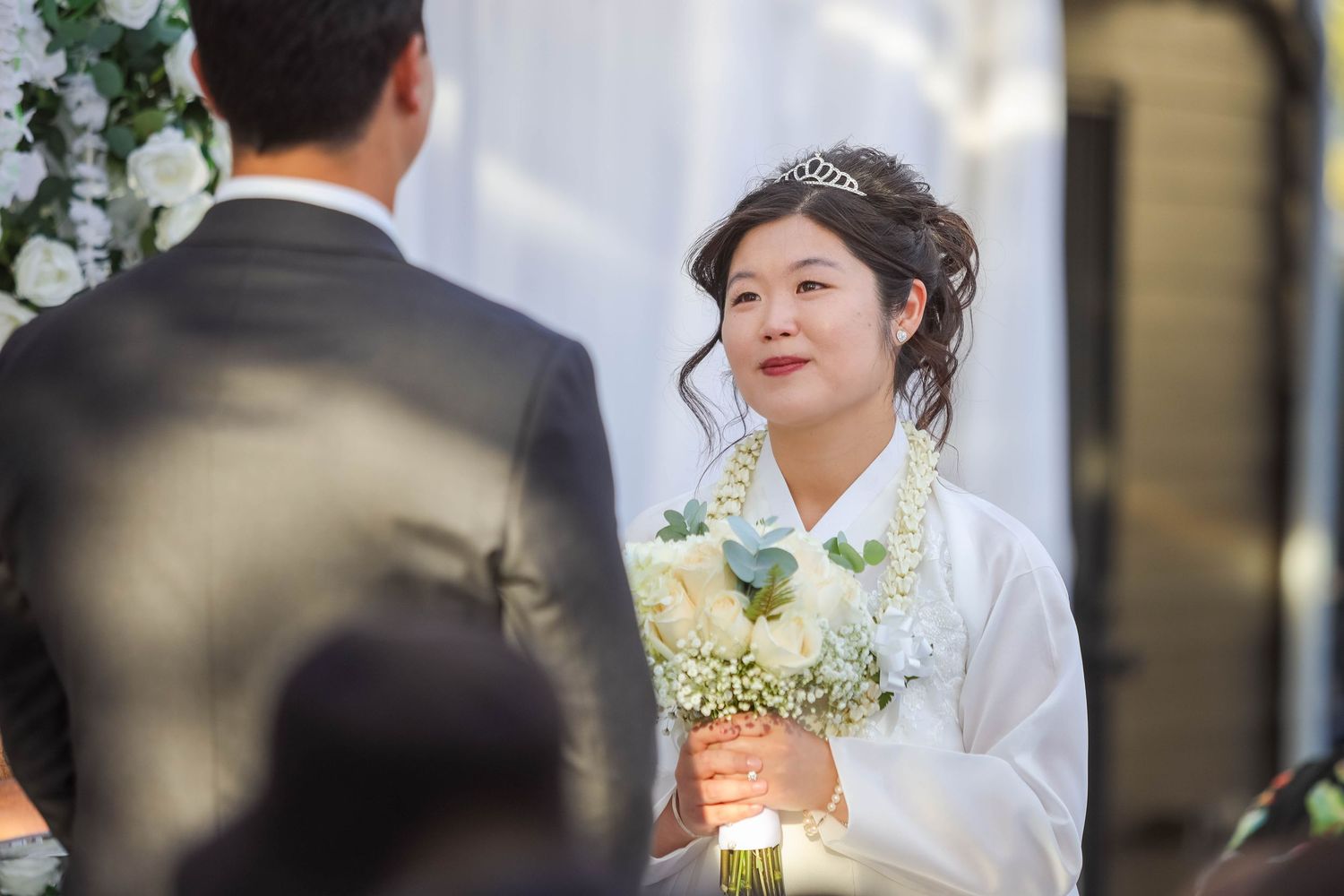 A bride and groom share intimate moments during their wedding ceremony surrounded by white floral decorations.
