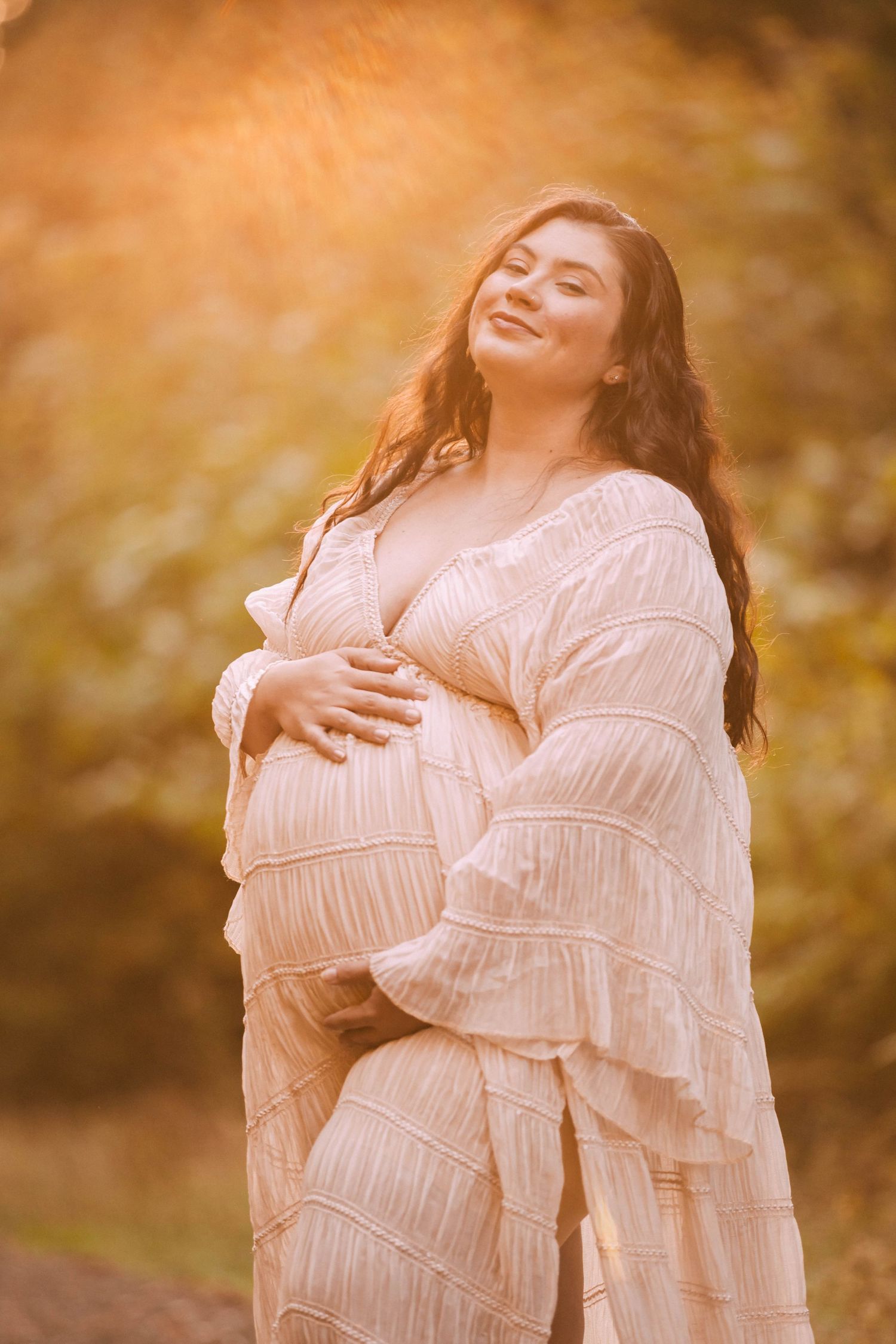 A woman in a white dress poses expressively against a warm autumn backdrop during golden hour.