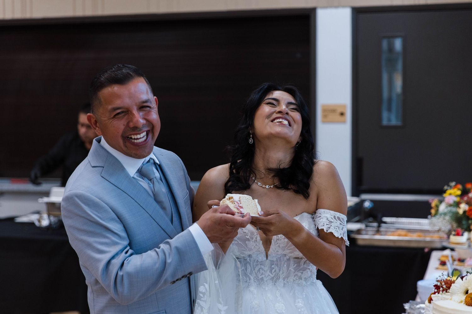 Wedding couple shares joyful laughter during reception celebration at indoor venue.