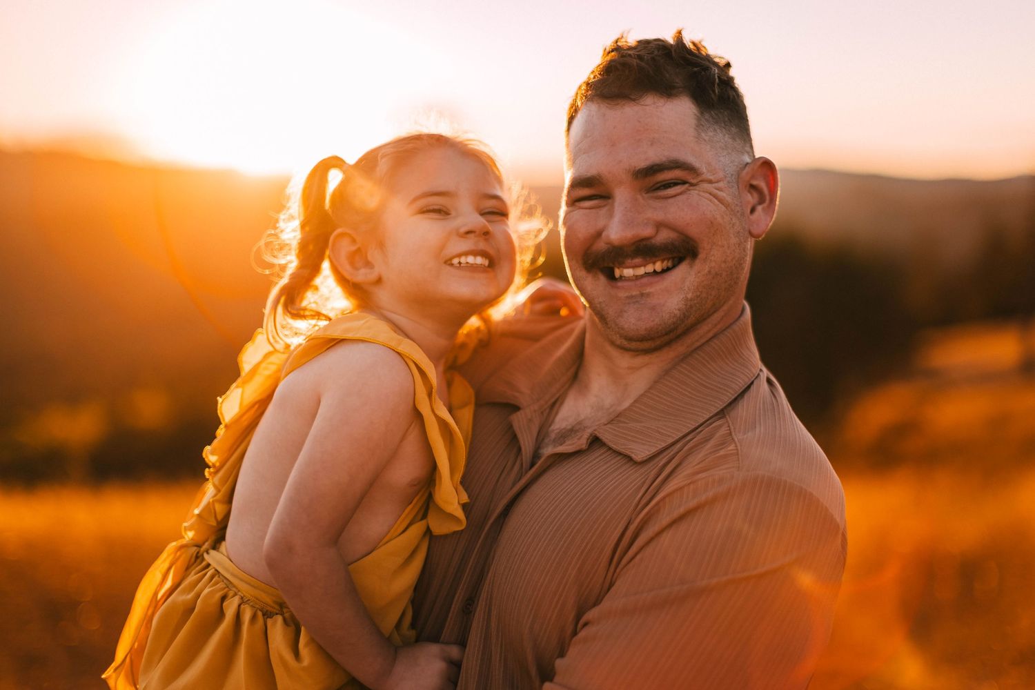 A couple embraces in a golden field during sunset while wearing brown and yellow outfits.