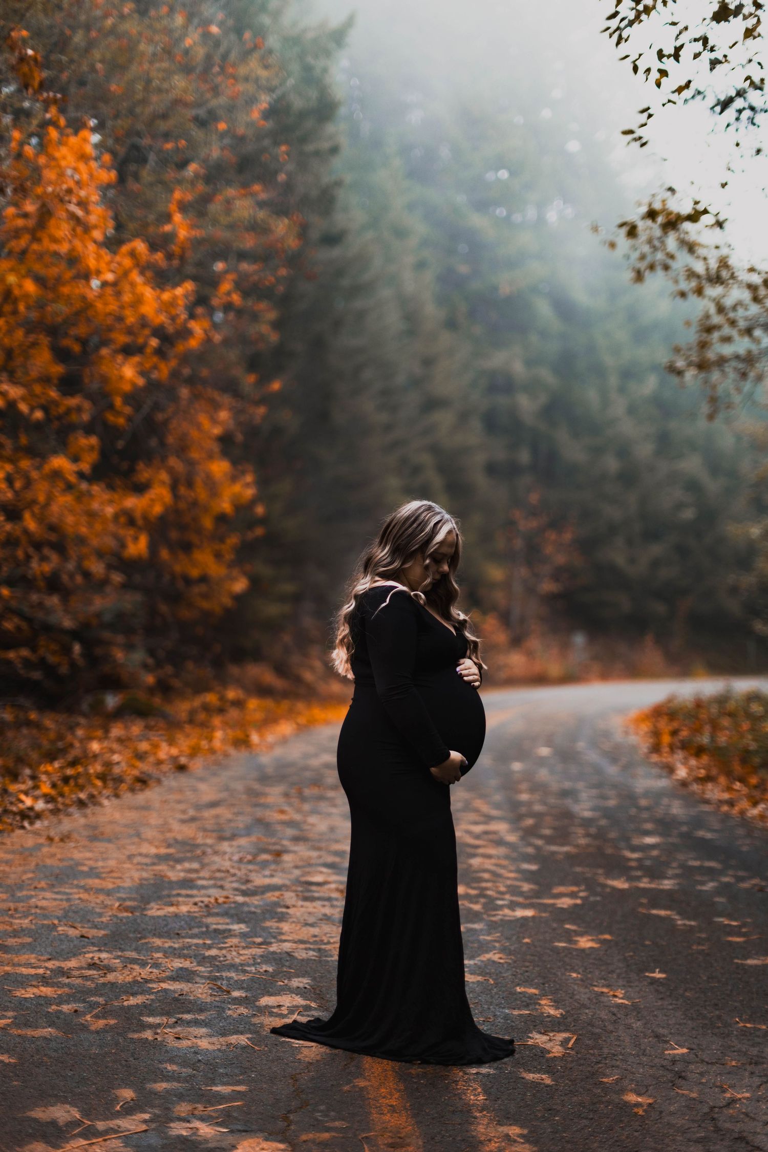 A figure in a black dress sits on an autumn path surrounded by vibrant orange leaves and misty forest atmosphere.