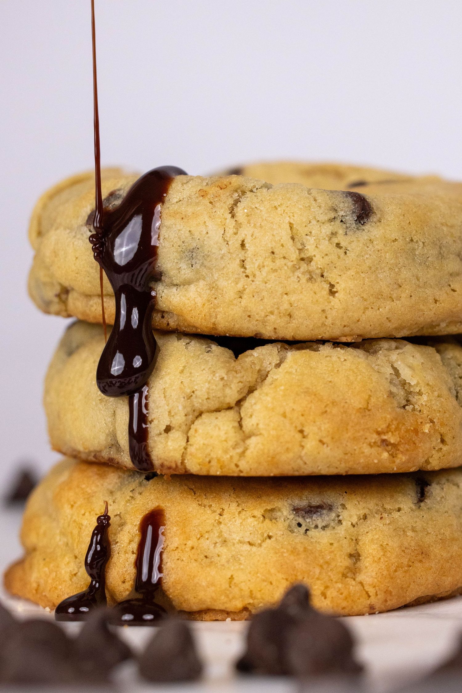 Stack of chocolate chip cookies with melted chocolate drizzle on top and chocolate chips scattered around.