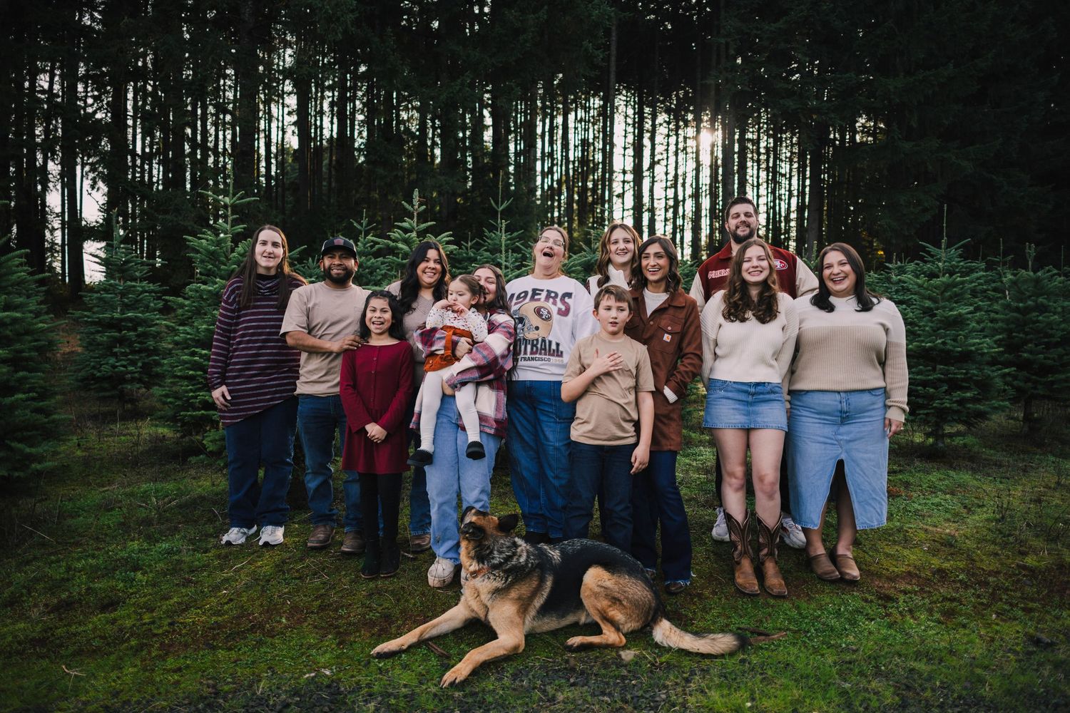 A group of people in casual attire gather together for photos in a wooded forest setting.