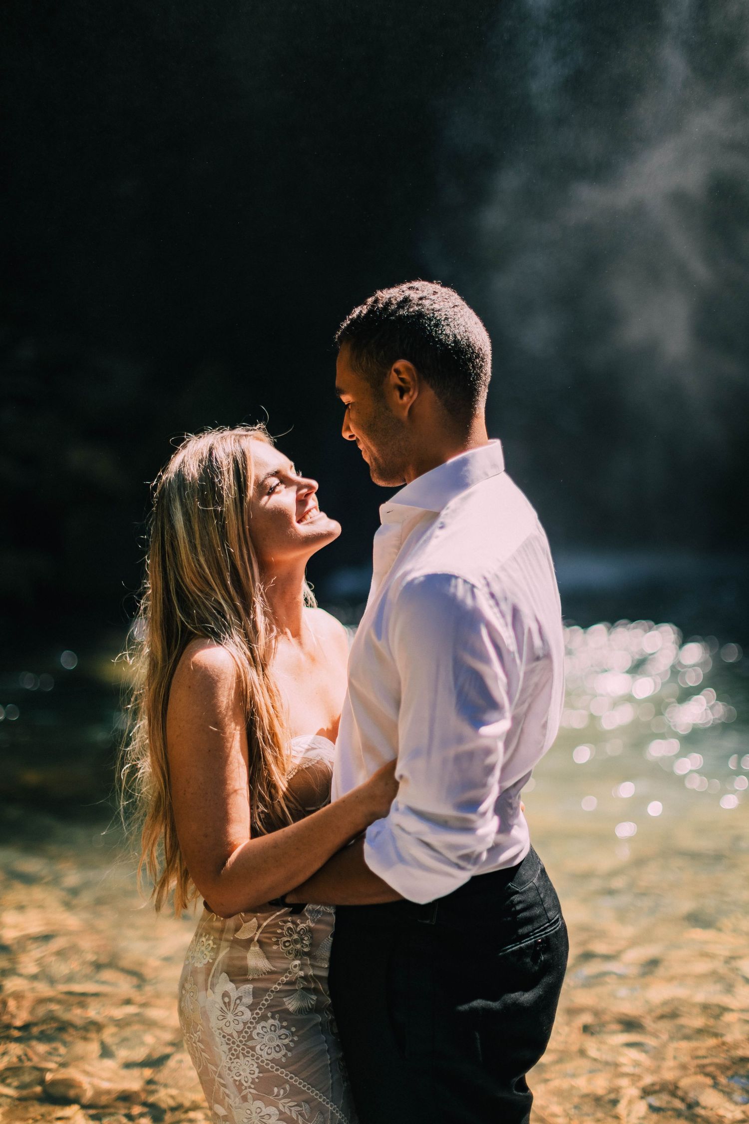 A romantic couple embraces in dreamy golden sunlight by a misty lake creating an ethereal wedding photograph.