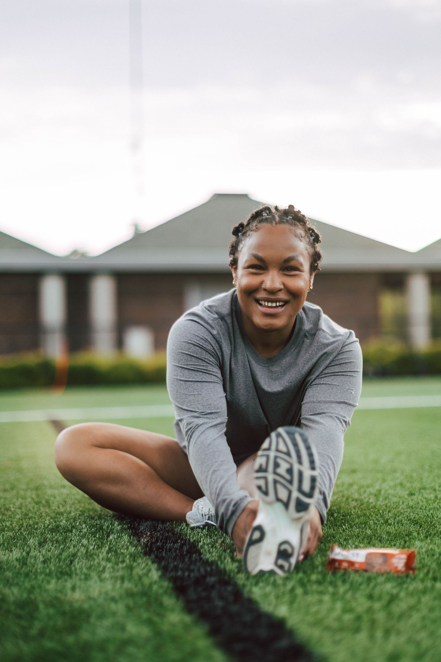 Person in gray top stretches on green grass field during outdoor fitness workout session.