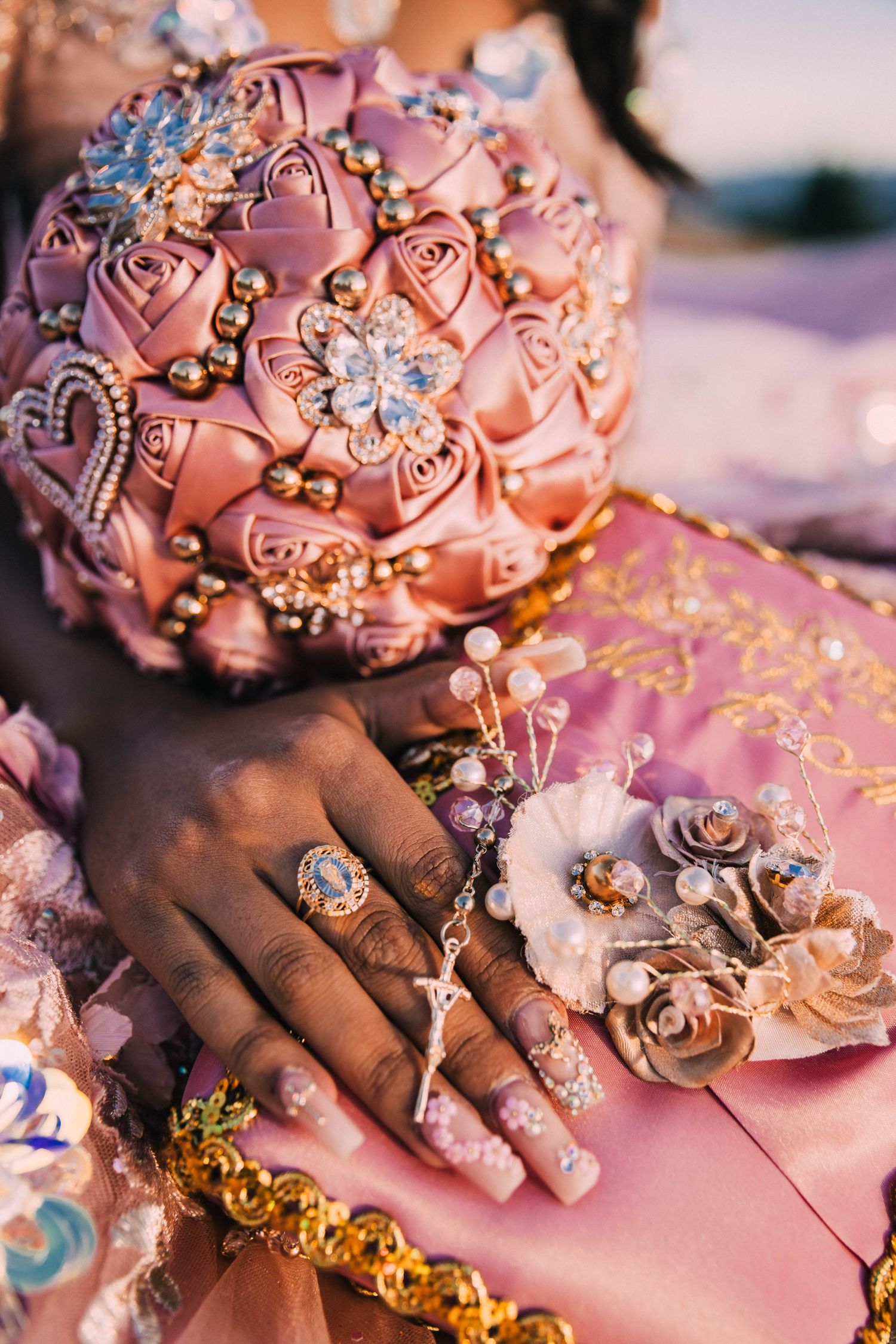 Ornate pink bridal bouquet with crystal embellishments and jewelry details shown alongside decorated hands with manicured nails.