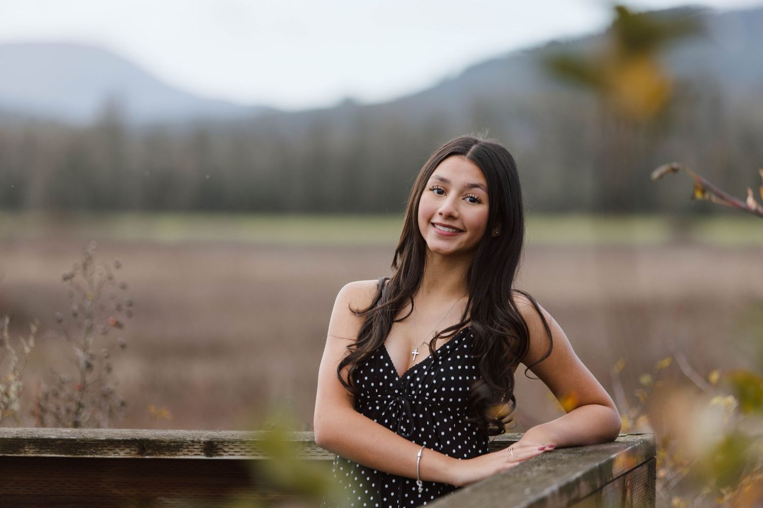 A woman in a polka dot dress poses outdoors in a natural setting during golden hour.