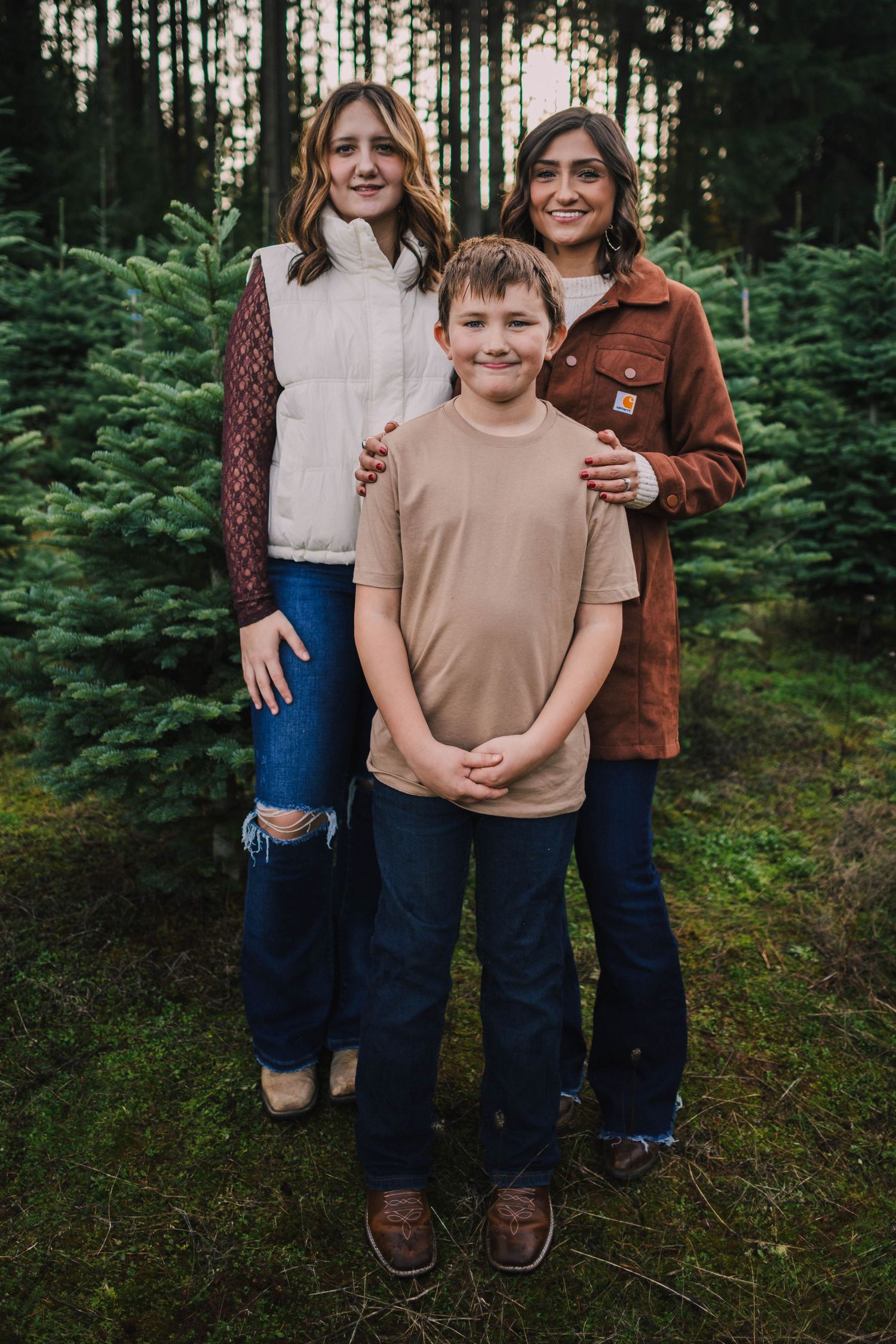 A family poses together in a lush evergreen forest setting wearing casual fall clothing.