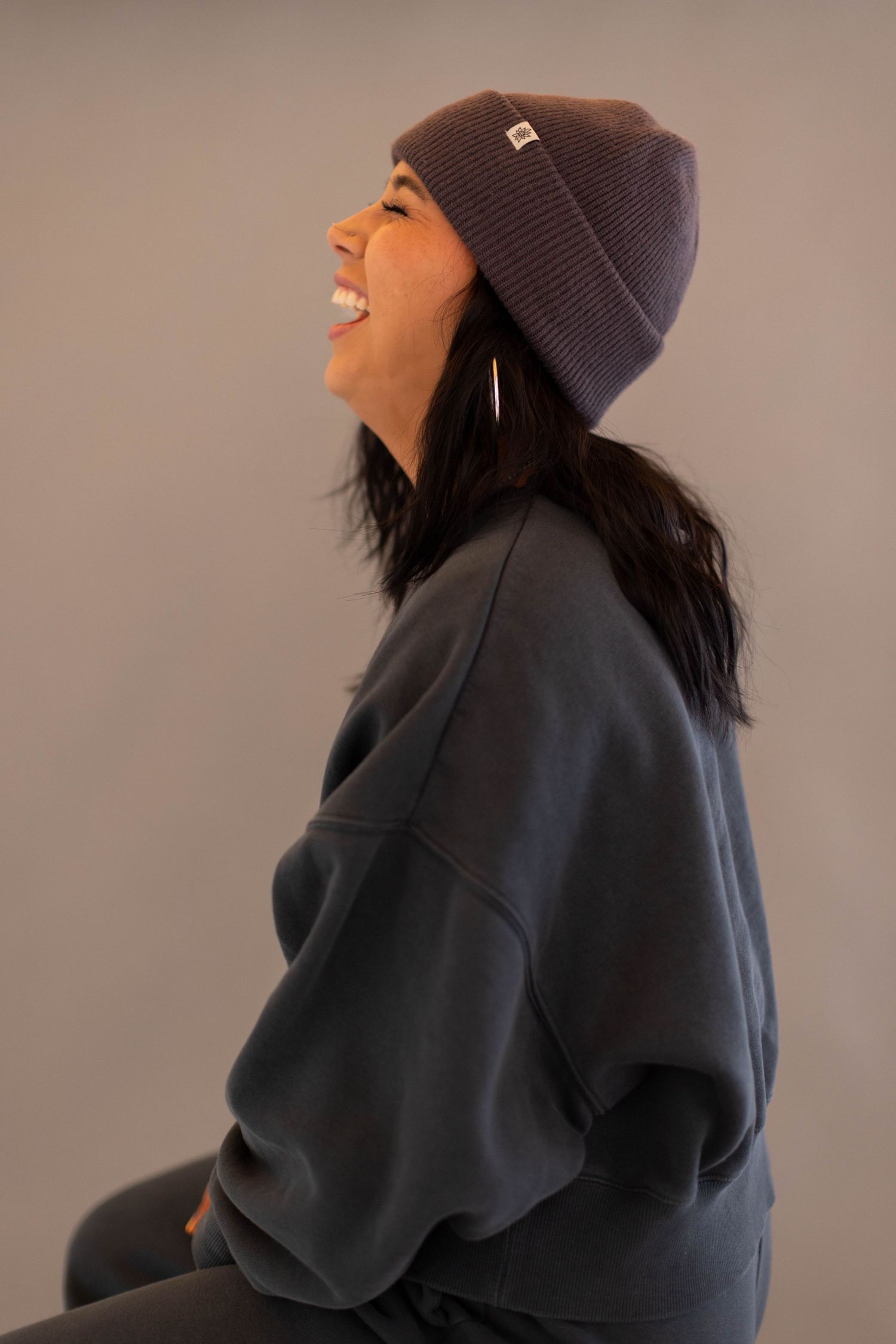 A person wearing a dark beanie and coat laughs joyfully in a series of candid profile shots against a neutral background.