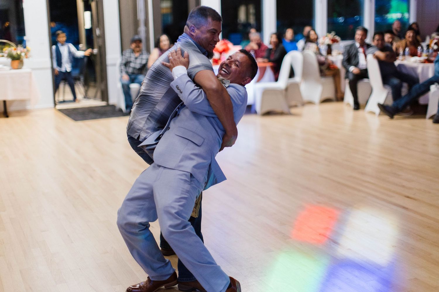 A person in a gray suit performs an energetic breakdance move on a polished floor during a celebration.