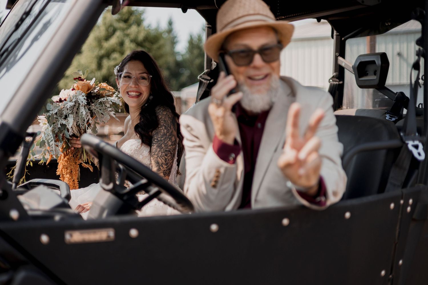 A couple in formal wedding attire sits together in a vintage car during their wedding celebration.