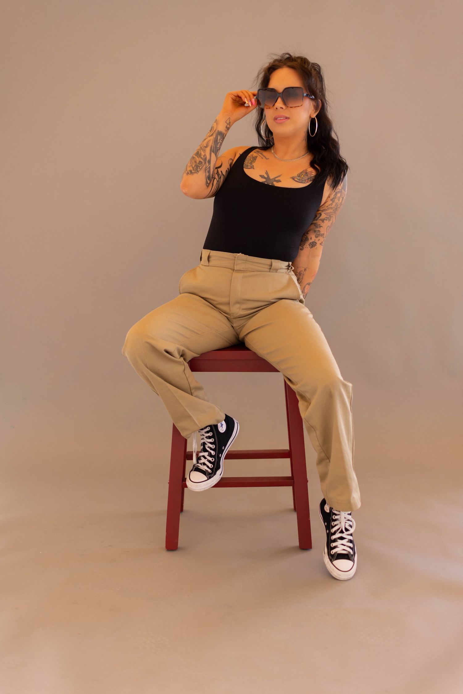 A series of fashion poses on a red wooden chair against a beige backdrop showcasing casual khaki pants and black top.
