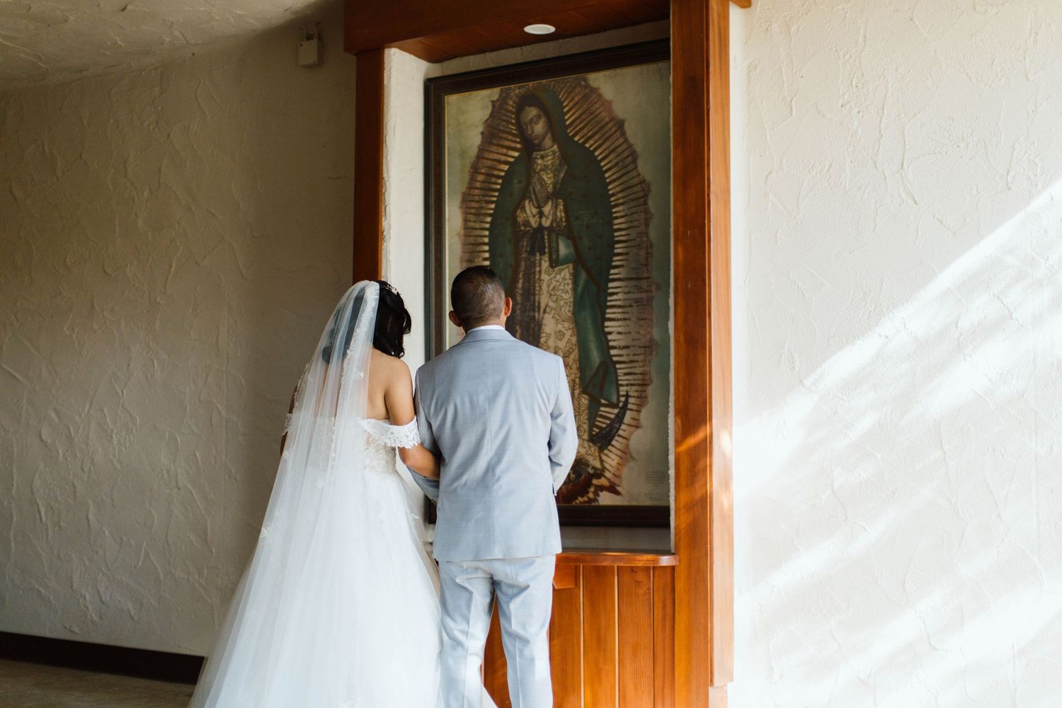 A couple in wedding attire enters through a wooden doorway with religious artwork visible on the wall.