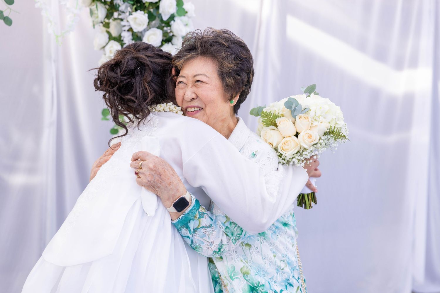 Wedding party members embrace during emotional moment at reception with white curtain backdrop.