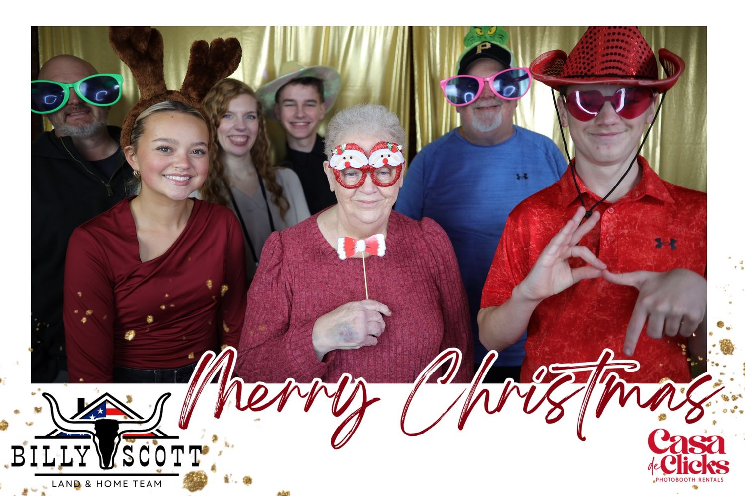 A group wearing festive props and holiday attire poses together for a Christmas photo booth picture with a Merry Christmas banner.