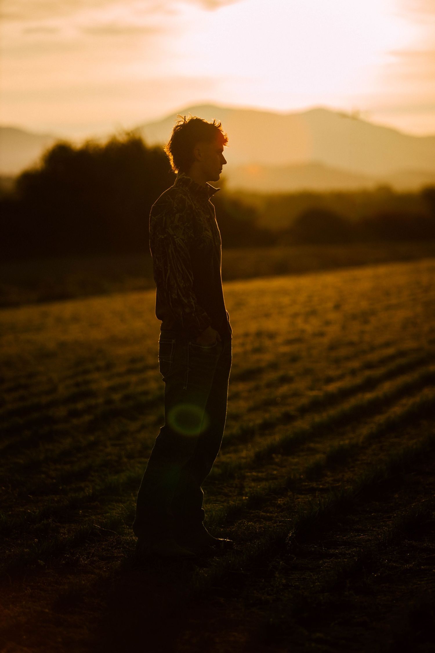 Silhouette of a person standing in a field at sunset with mountains in the background.