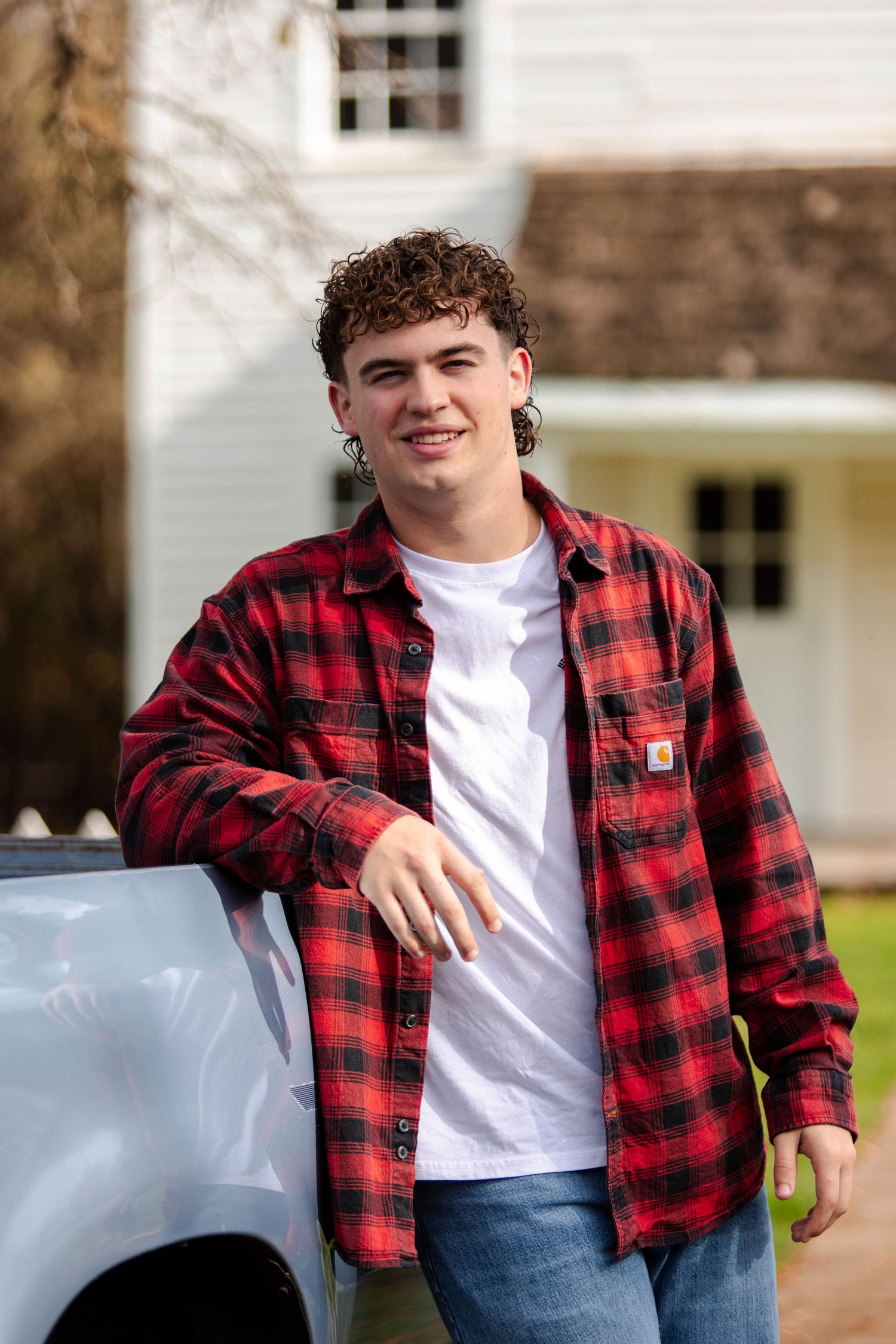 A person in a red buffalo plaid flannel shirt and white t-shirt poses casually outdoors.